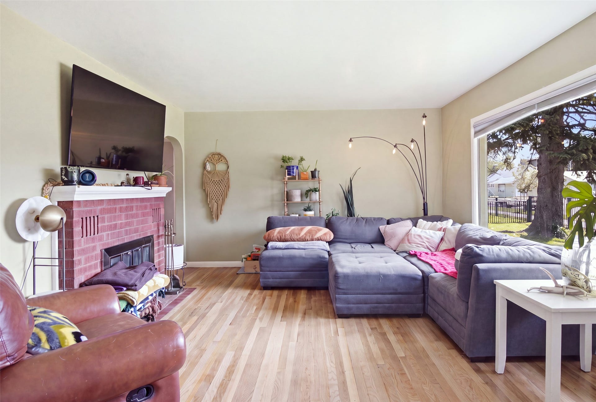 Spacious living area featuring light wood-finish flooring, a brick fireplace with a white mantel, and a large window