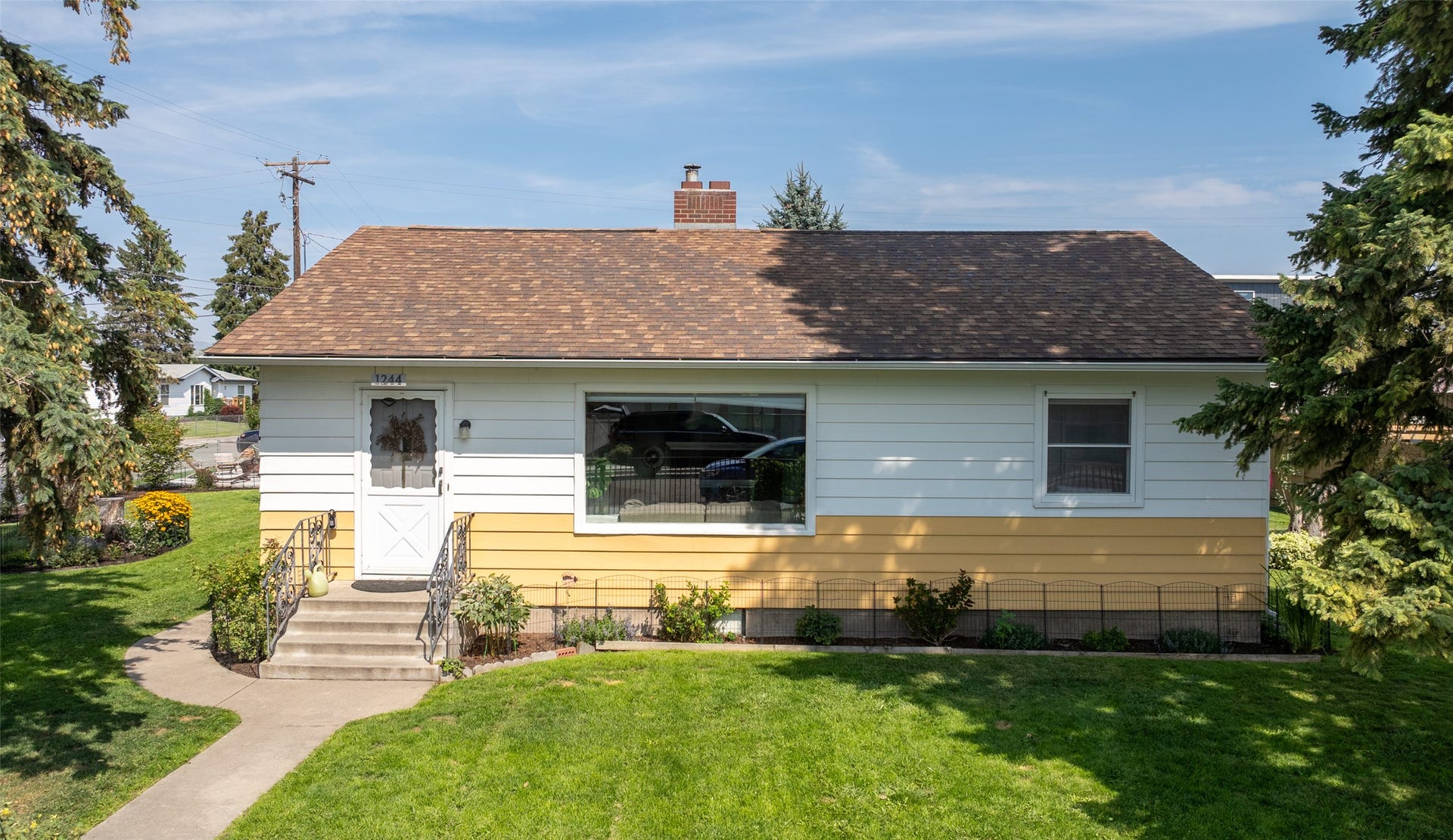 Ranch-style residence featuring a brown shingle roof, white and yellow siding, and a prominent front picture window