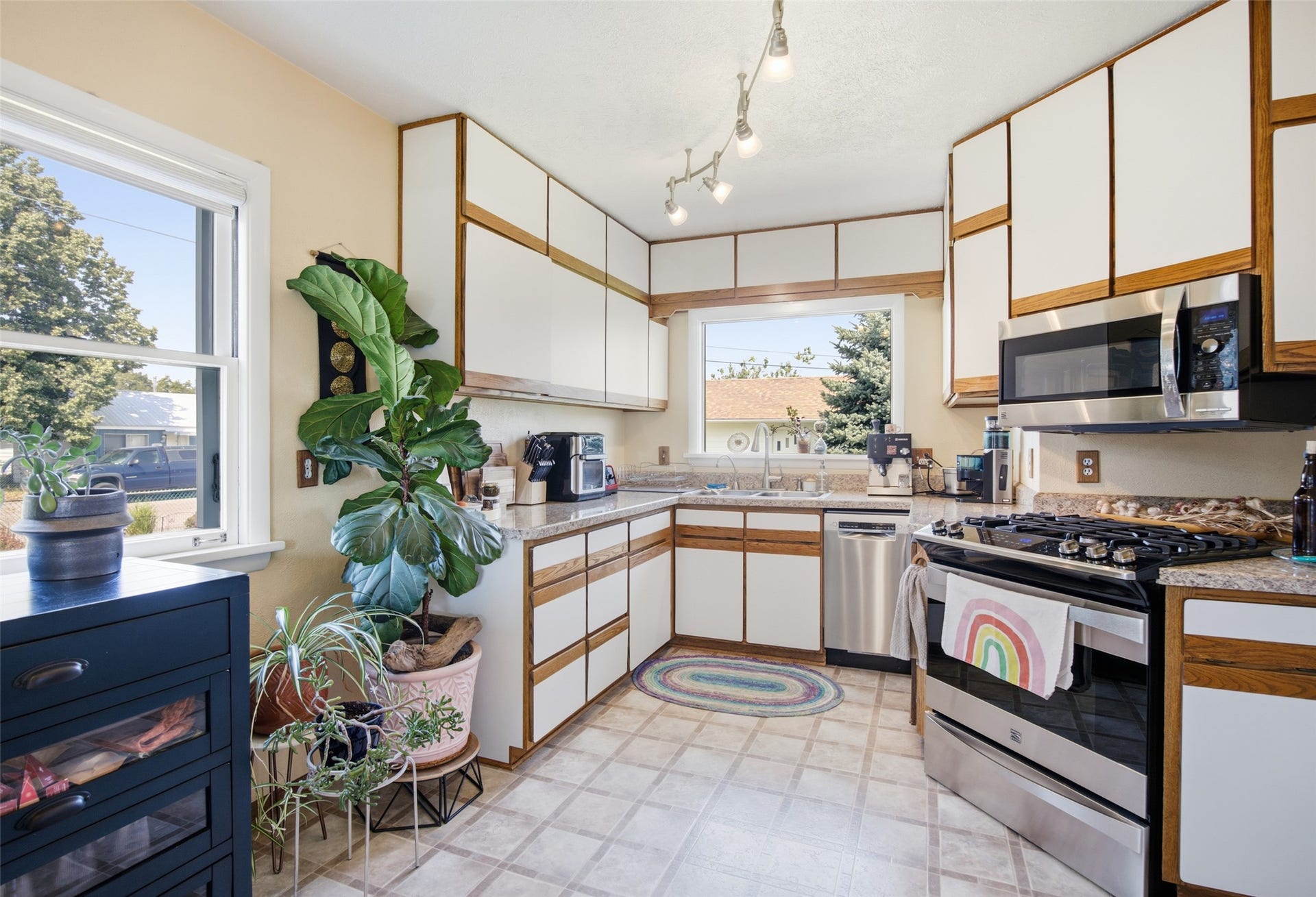 Kitchen featuring L-shaped counter space, built-in stainless steel appliances, white cabinetry with wood trim, track lighting, and a double window