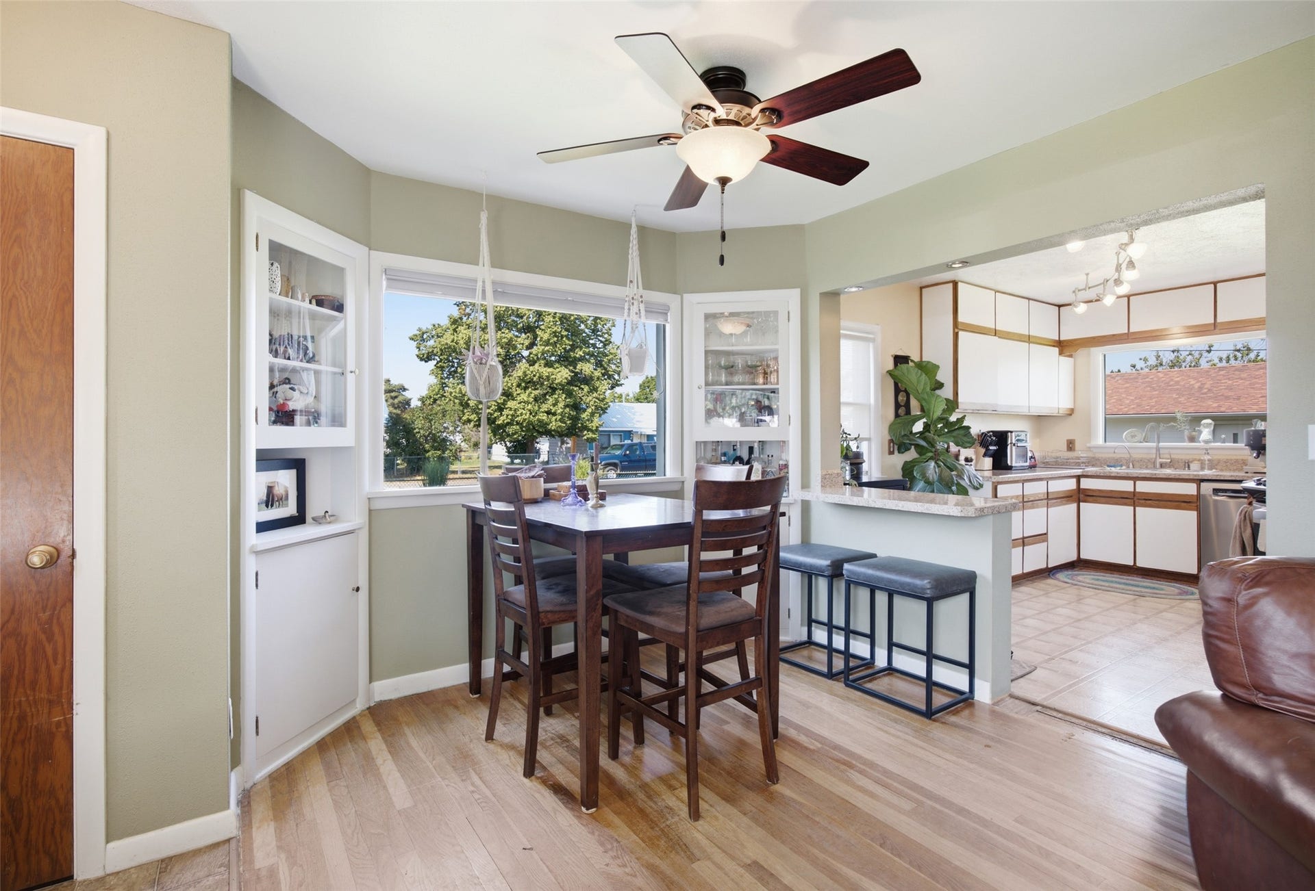 Hardwood flooring throughout, built-in display cabinetry, ceiling fan with integrated lighting, and a breakfast bar with stone-finish countertop