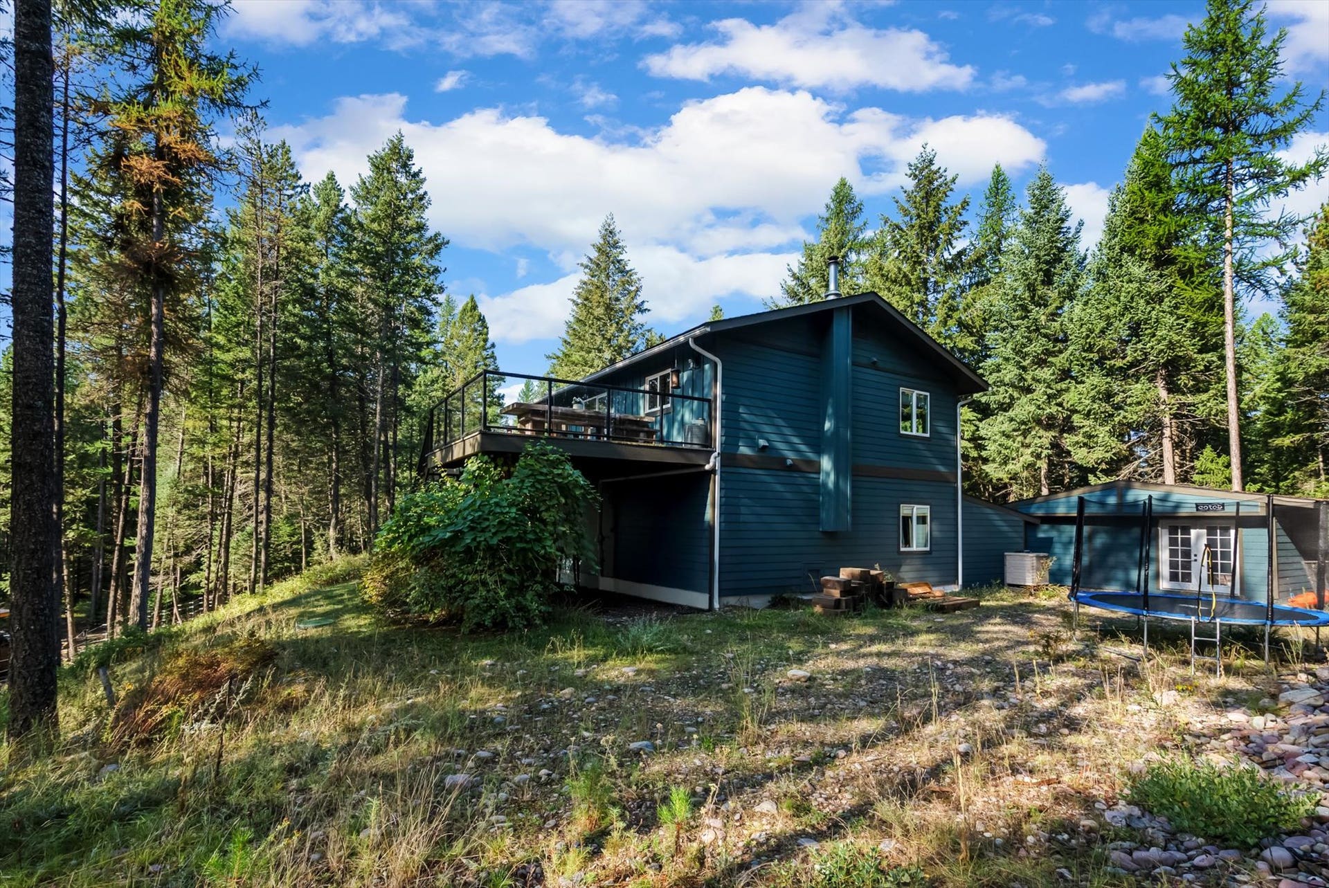 You'll love the newly painted exterior of this home that serves as a central hub for outdoor living. This view perfectly captures the secluded nature of the property, showing the home situated privately on 4.79 acres and illustrating the seamless connection between the interior and the stunning Montana landscape.