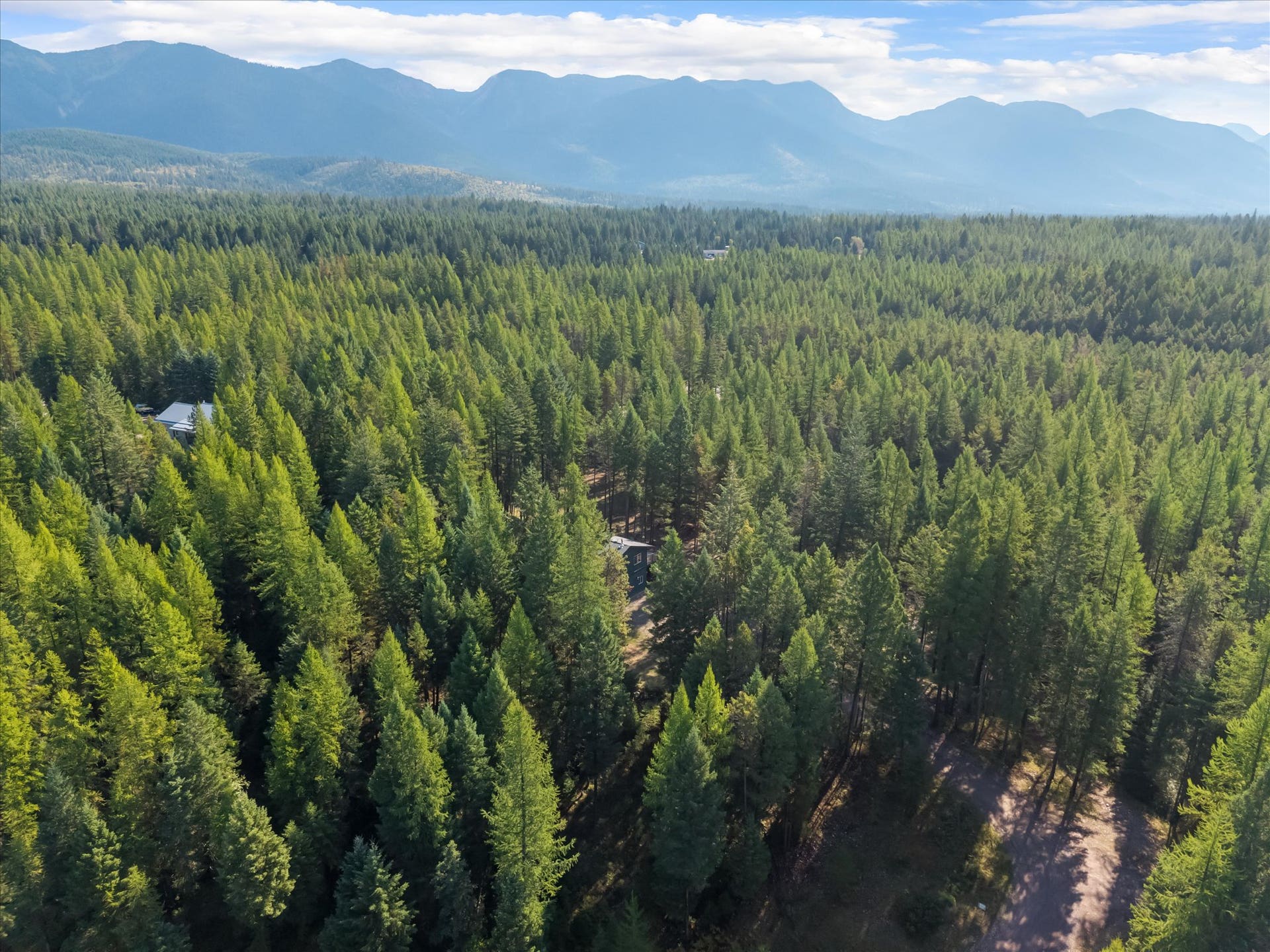 An outdoor enthusiast's paradise: Aerial view highlighting the private 4.79-acre property positioned directly along the Foothills Road corridor. Step out your front door to immediate access for summer hiking, mountain biking, and horseback riding, or explore nearby winter trails perfect for cross-country skiing and snowshoeing throughout the Flathead Valley.