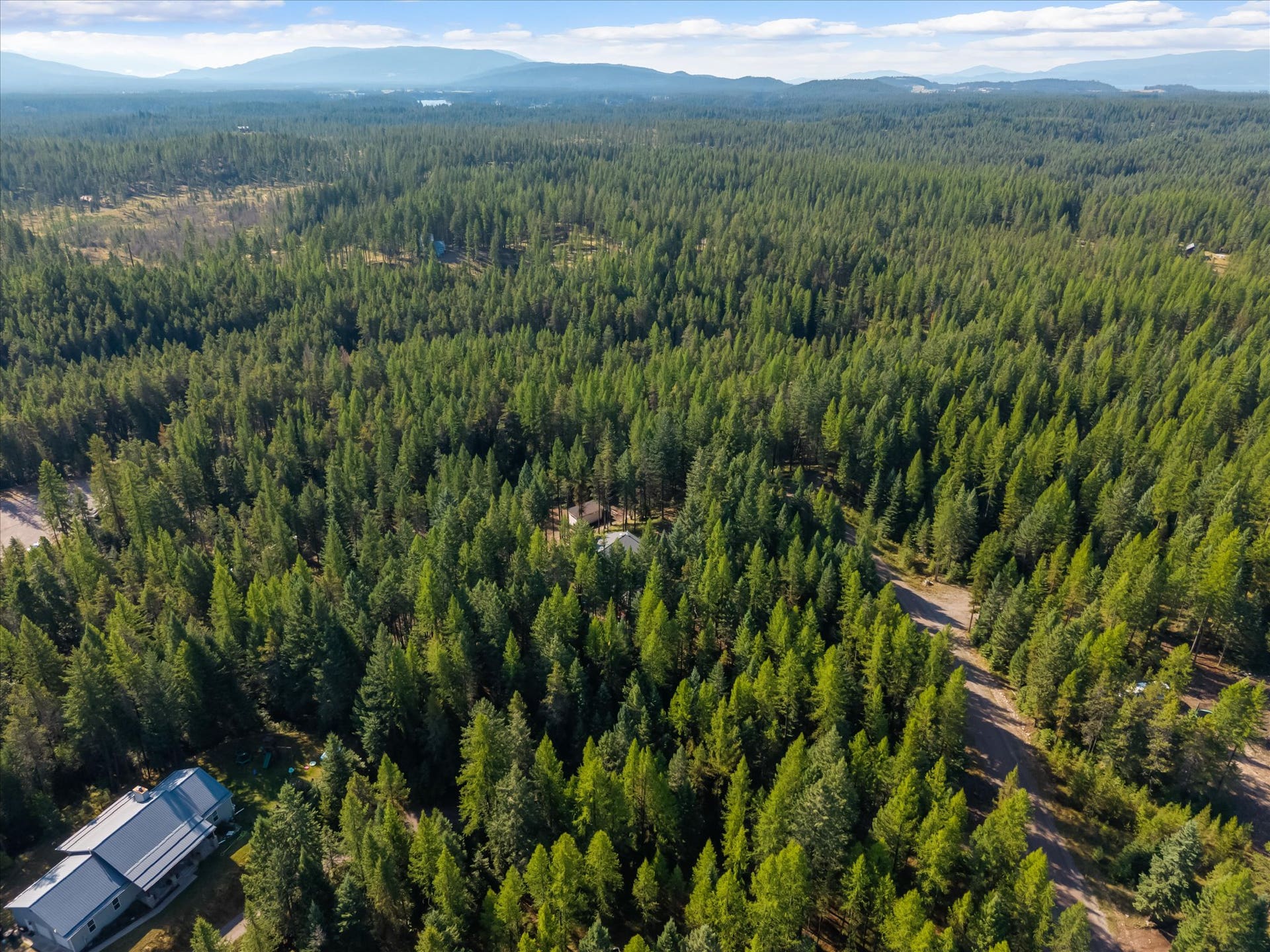 An outdoor enthusiast's paradise: Aerial view highlighting the private 4.79-acre property positioned directly along the Foothills Road corridor. Step out your front door to immediate access for summer hiking, mountain biking, and horseback riding, or explore nearby winter trails perfect for cross-country skiing and snowshoeing throughout the Flathead Valley.