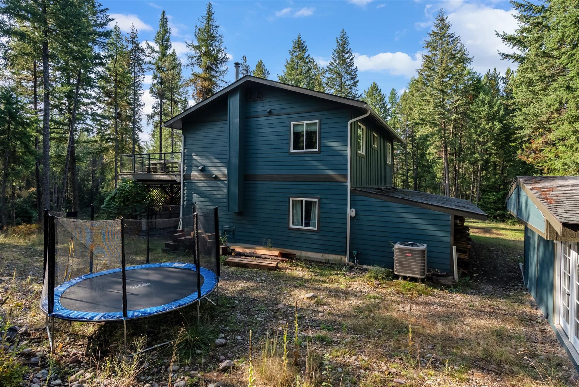 You'll love the newly painted exterior of this home that serves as a central hub for outdoor living. This view perfectly captures the secluded nature of the property, showing the home situated privately on 4.79 acres and illustrating the seamless connection between the interior and the stunning Montana landscape.
