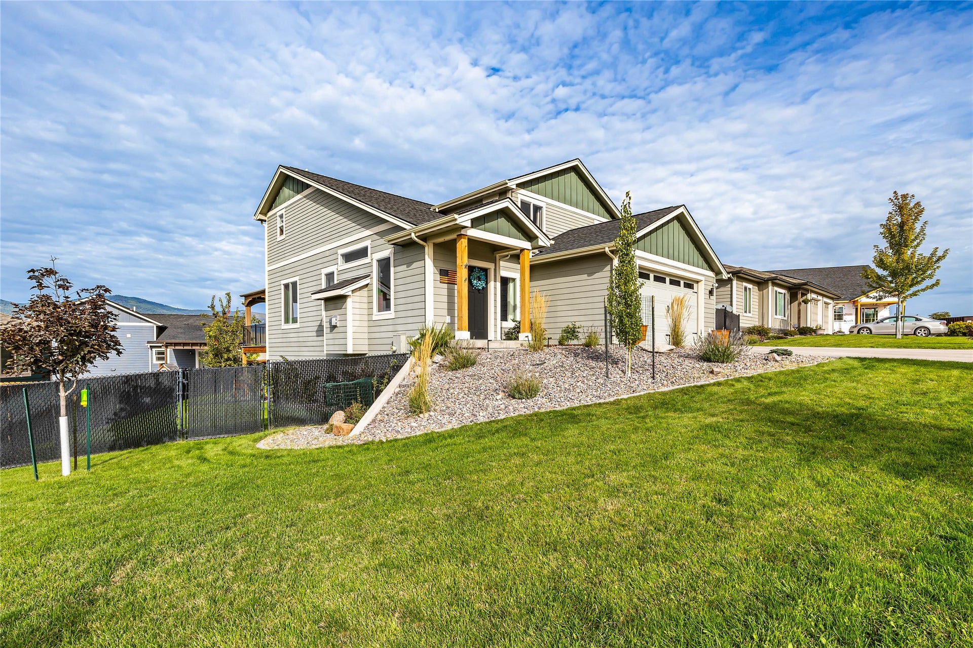 Contemporary exterior with green gables, light gray siding, an attached garage, and a sloped front yard with a landscaped rock bed