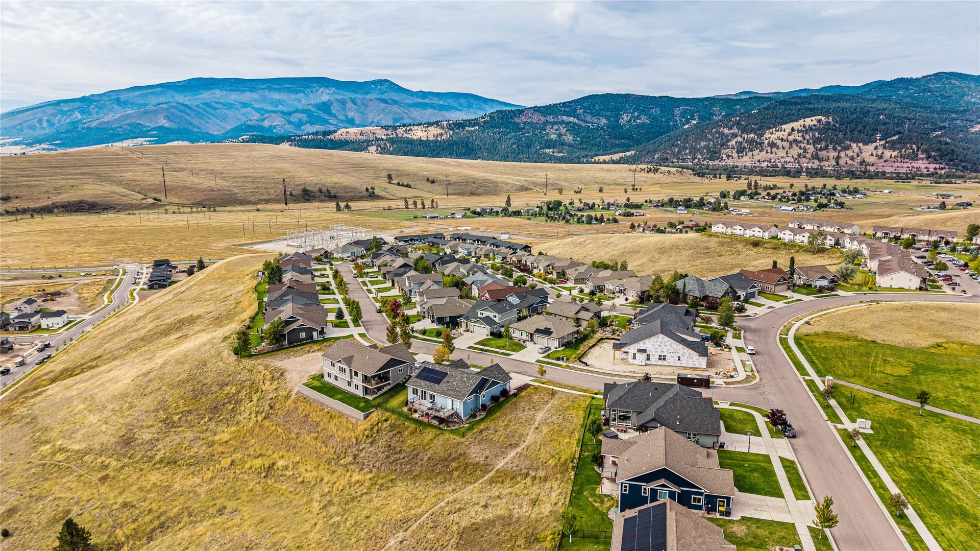 Residential neighborhood with paved streets and sidewalks, surrounded by rolling hills and distant mountains