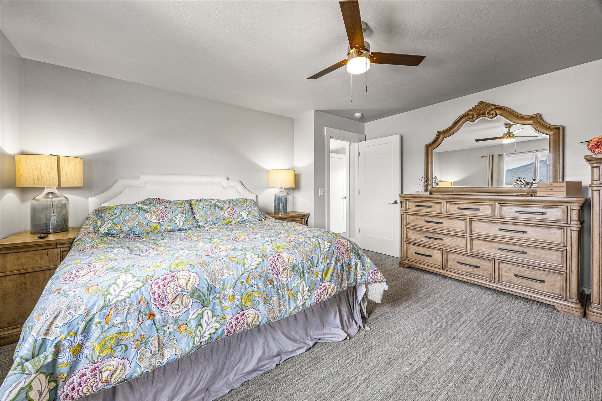Light gray wall paint, textured gray carpeting, white interior doors, and a wood-finish ceiling fan