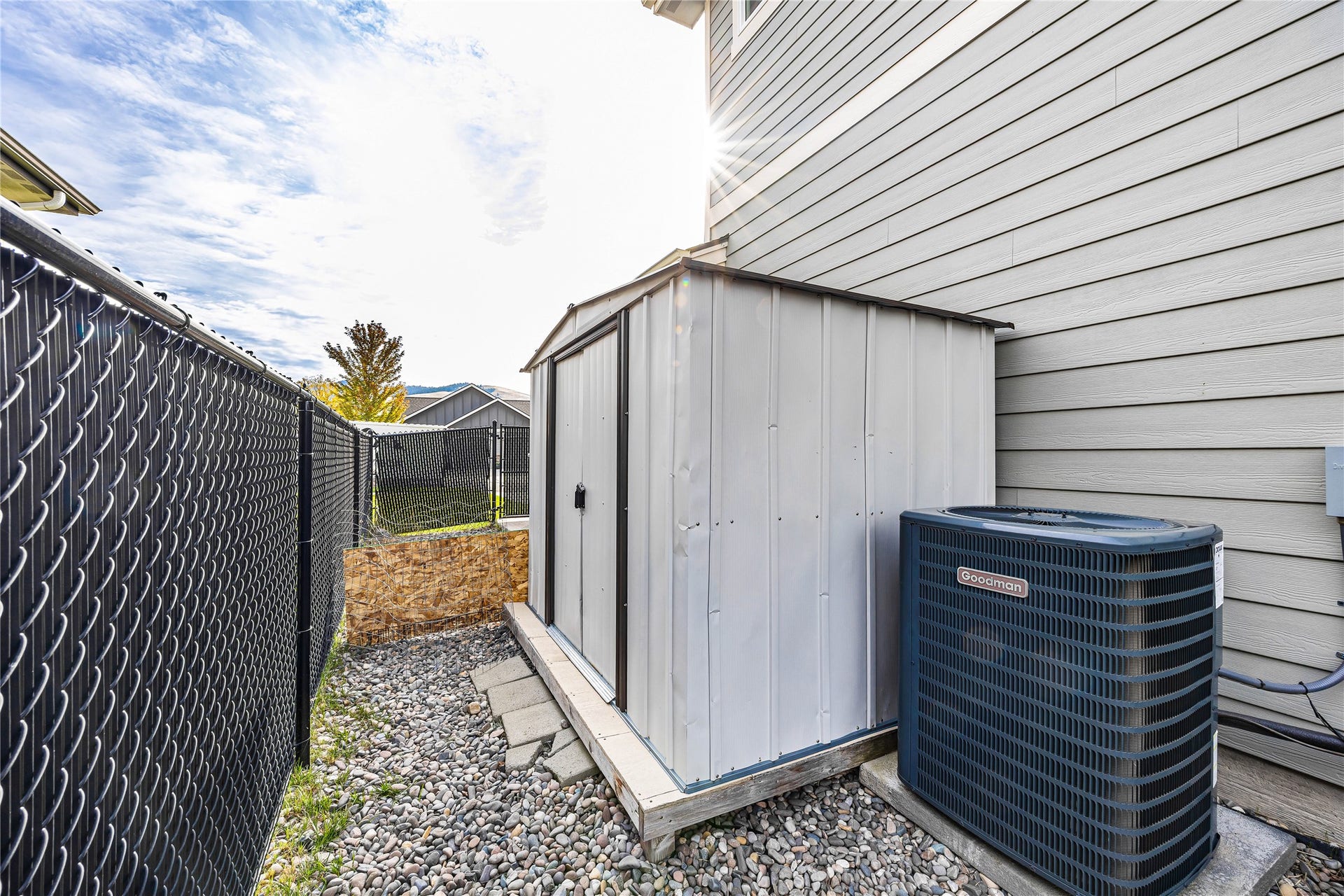 Metal storage shed on a raised platform, gravel groundcover, and chain link fencing