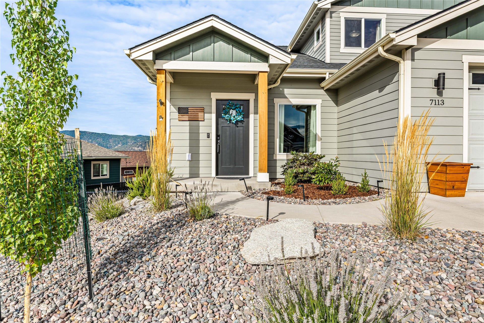 Exterior siding, covered porch entry, wood-finish columns, concrete walkway, and gravel landscaping