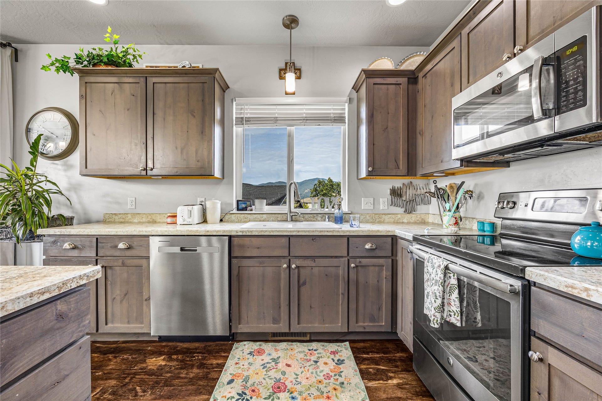 U-shaped kitchen with wood-finish cabinetry, light-toned countertops, and a stainless steel appliance suite including a dishwasher, range, and microwave