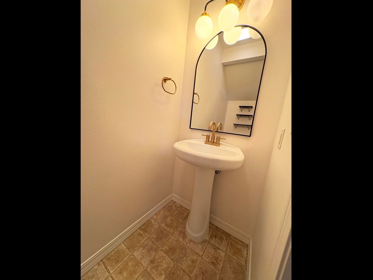 Pedestal sink with brass-finish faucet, arched mirror, and multi-bulb vanity lighting
