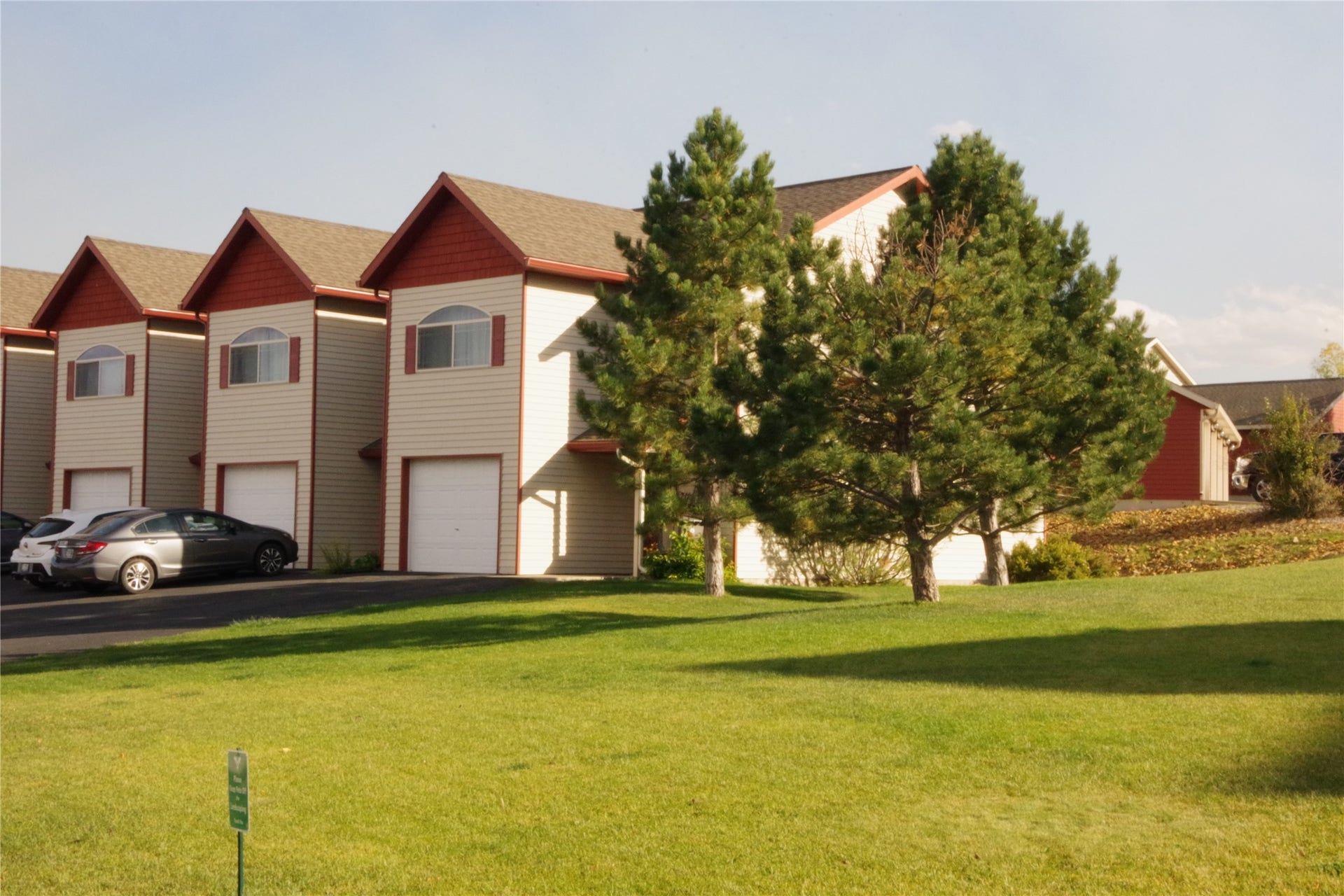711 Sonoma Drive, Helena, MT 59601 Exterior featuring light-colored siding with red gables, individual garage doors, arched windows, and mature trees
