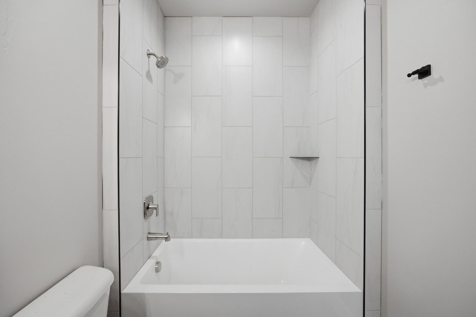 Bathtub with full-height tile surround, integrated shower niche, and chrome fixtures