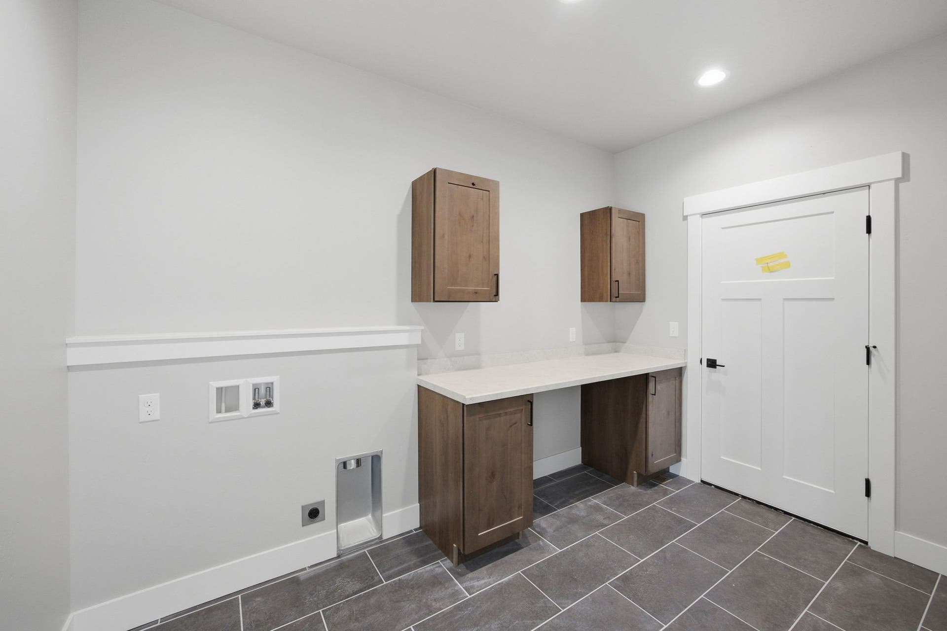 Laundry area featuring wood-finish cabinetry, light-toned countertop, recessed lighting, and gray tile flooring