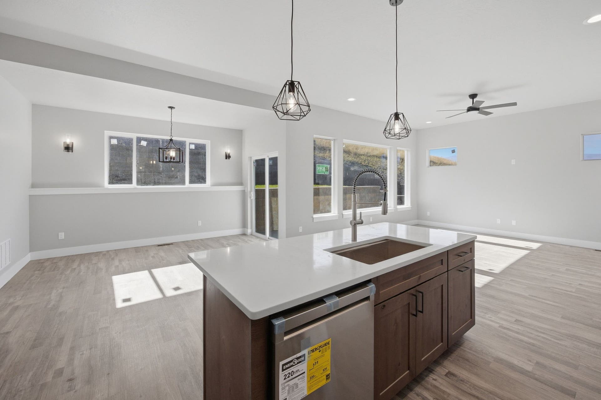 Open-concept living area featuring wood-finish flooring, a kitchen island with a built-in sink and dishwasher, pendant lighting, and multiple windows