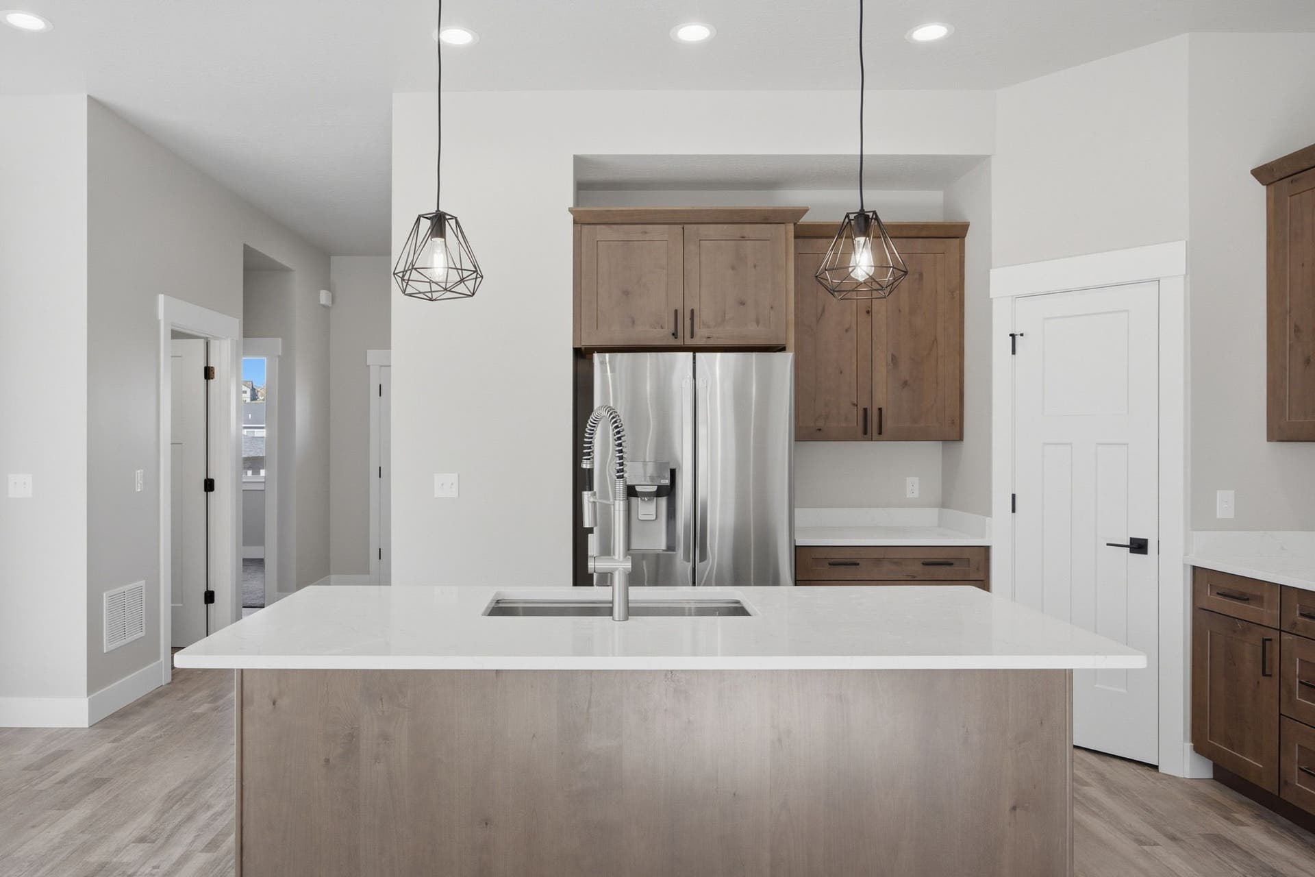 Kitchen featuring a large island with an undermount sink, stainless steel refrigerator, wood-finish cabinetry, recessed lighting, and pendant lighting