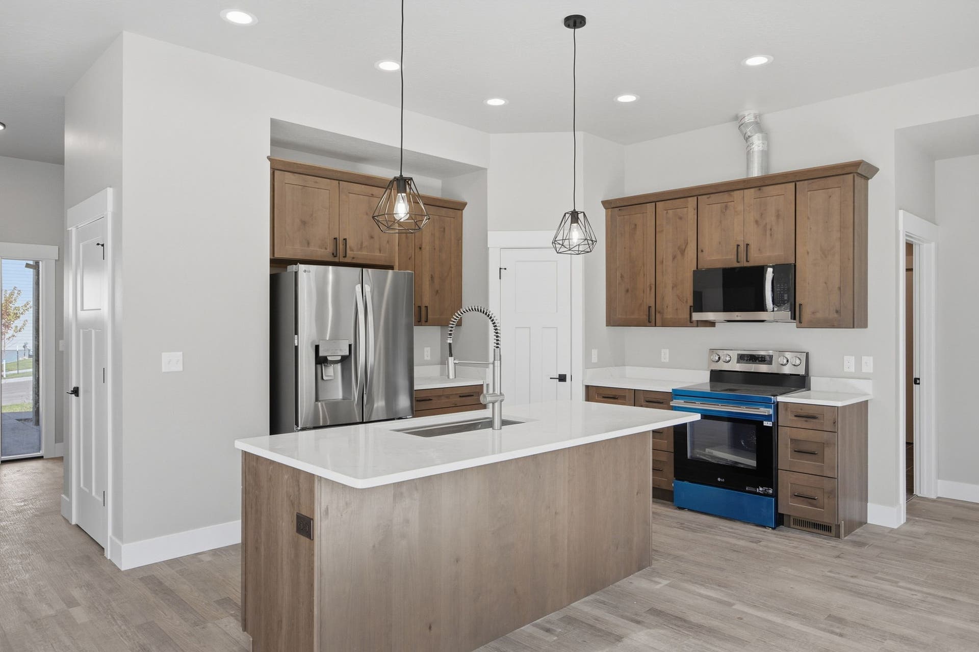 Kitchen featuring a central island with an undermount sink, pendant lighting, stainless steel appliances, wood-finish cabinetry, and light-toned countertops