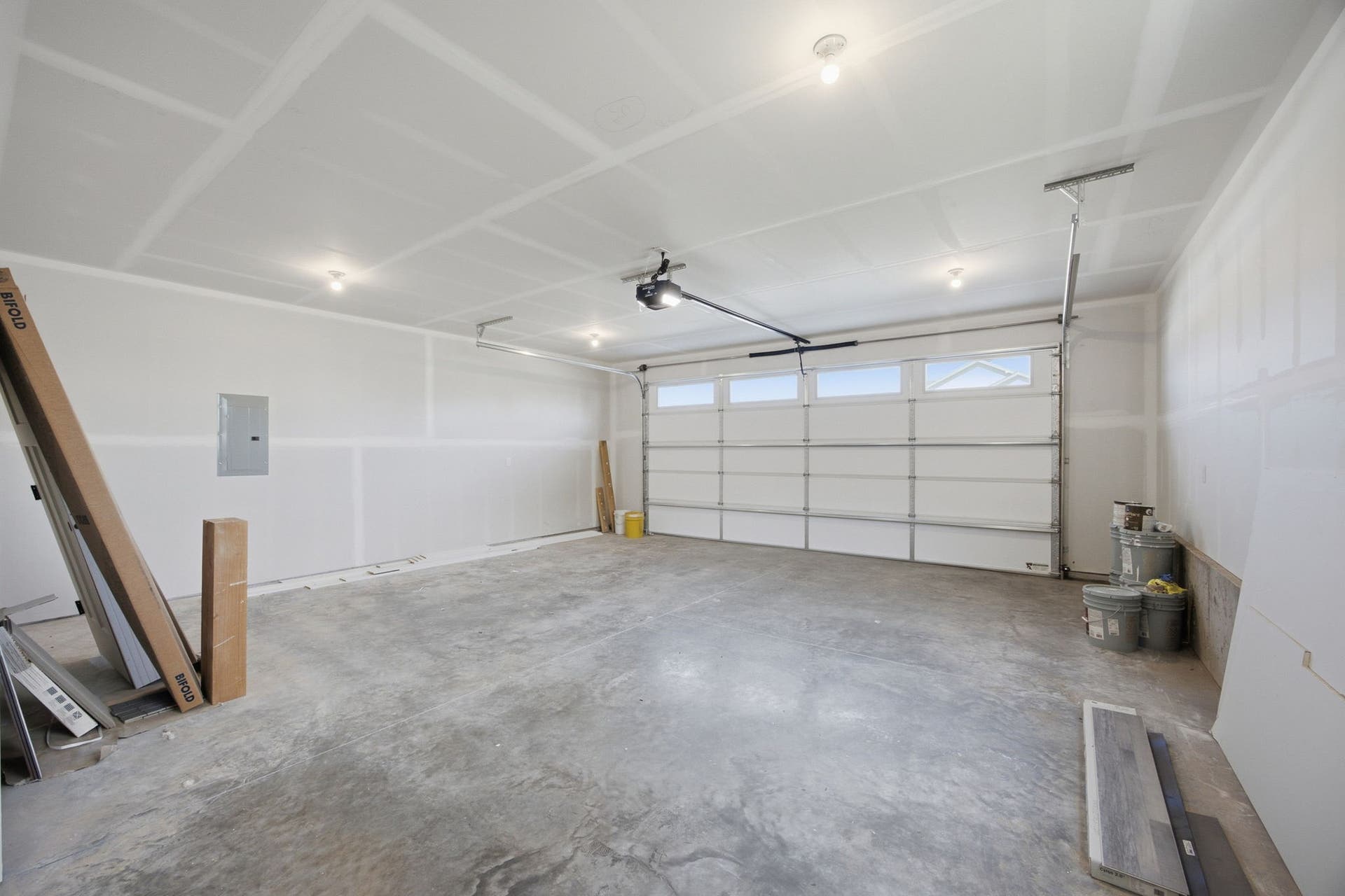 Spacious garage with an overhead door featuring upper window panels, concrete flooring, and ceiling-mounted lighting fixtures