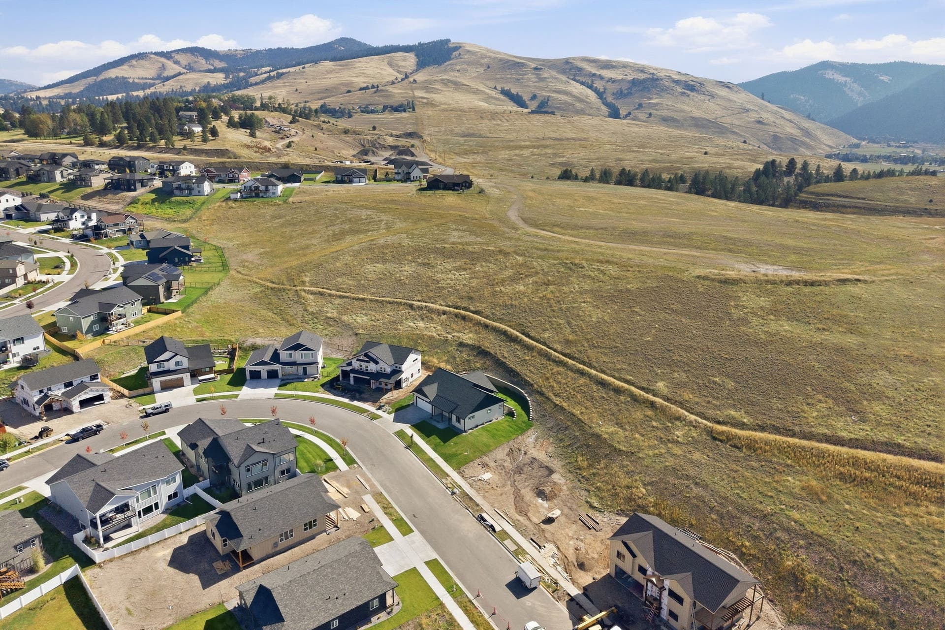 Mountainous backdrop, residential development, paved streets, varied architectural styles, natural grassy terrain