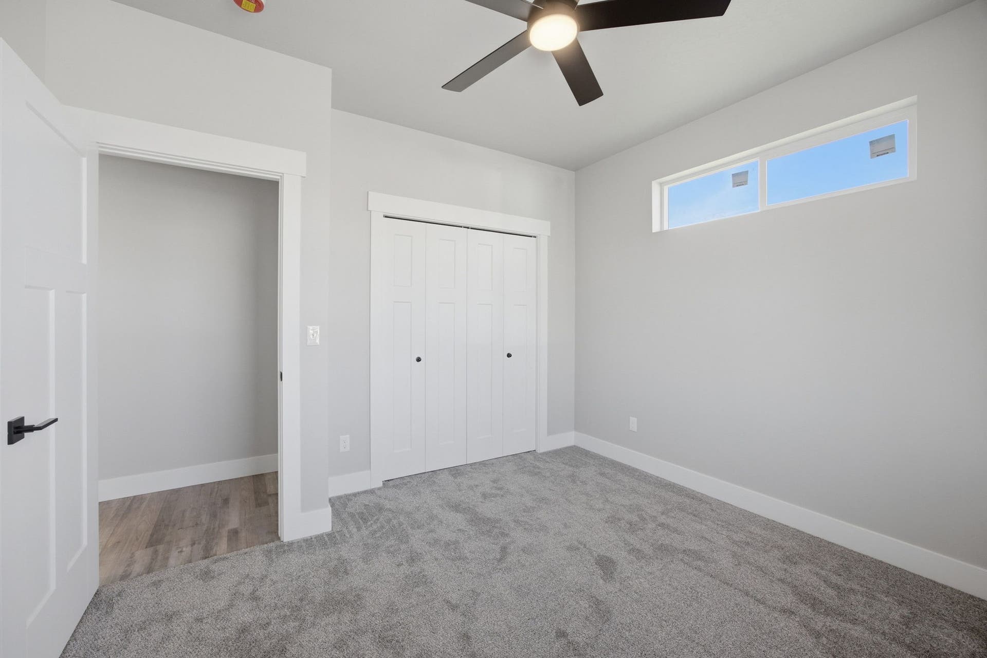 Recessed horizontal window, ceiling fan with integrated lighting, bi-fold closet doors, white trim, and light gray carpet