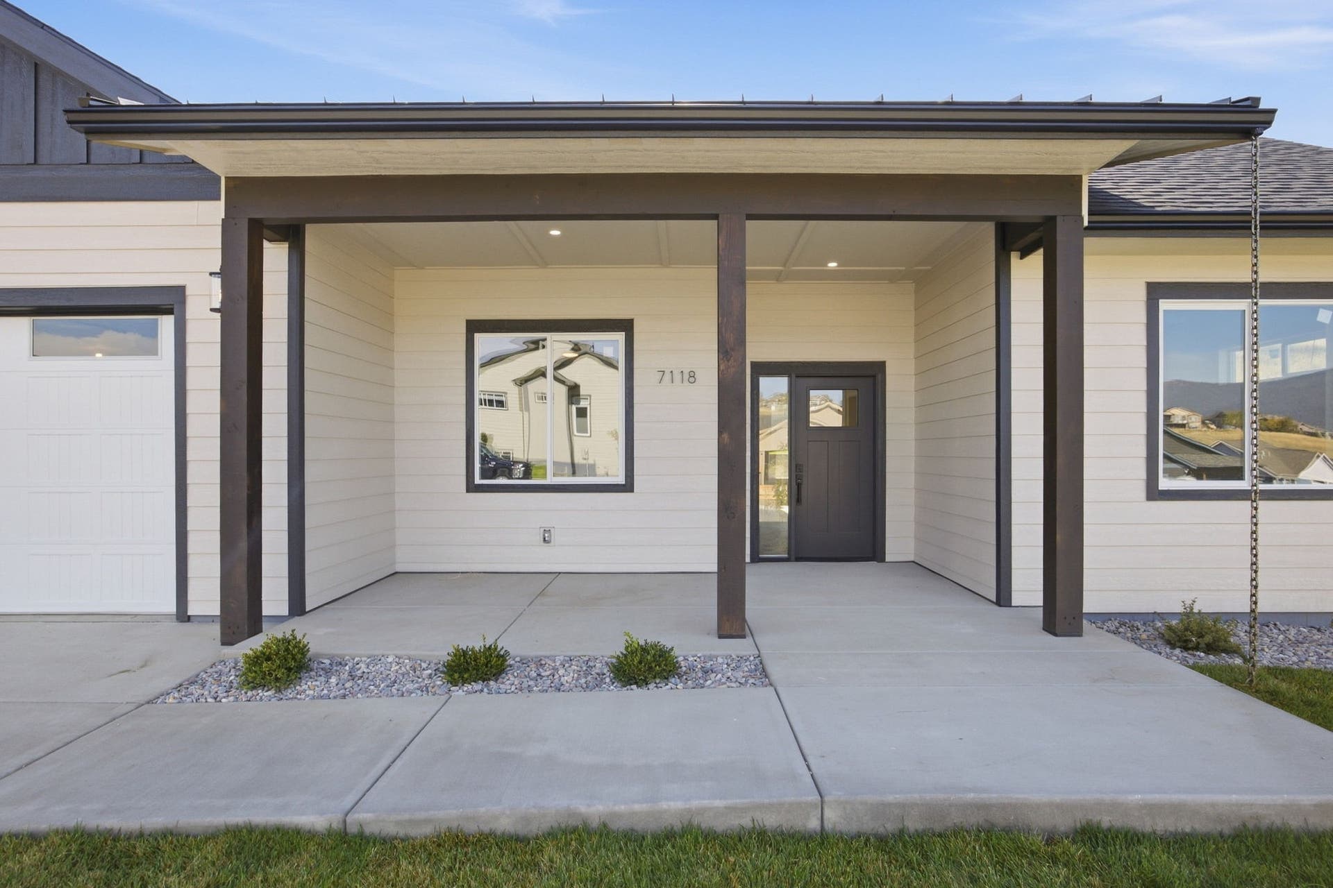 Covered entry porch with dark wood-finish columns, light horizontal siding, and a dark entry door with a sidelight