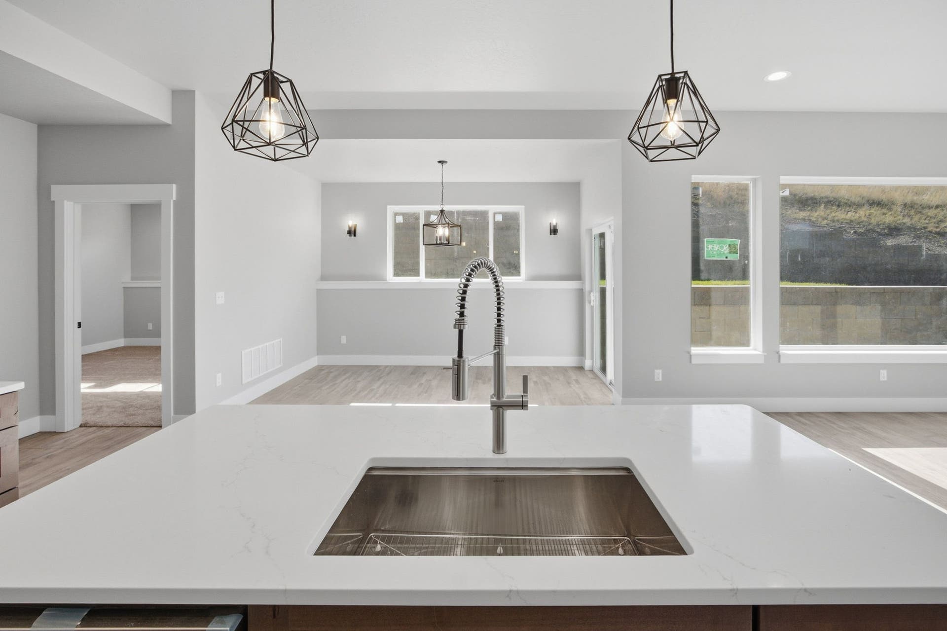 Open concept kitchen featuring a large island with an undermount sink and pull-down faucet, geometric pendant lighting, and light wood-finish flooring