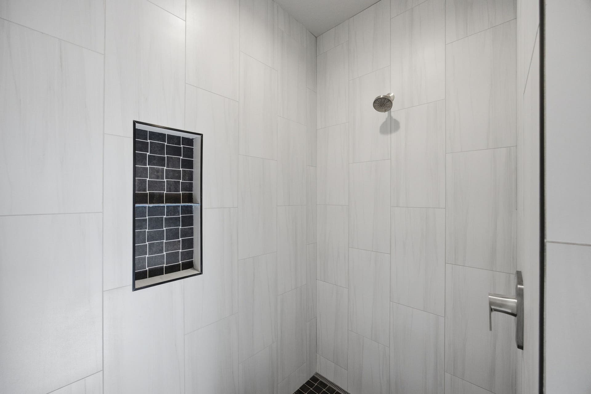 Shower with light-toned rectangular wall tiling, a built-in niche featuring dark mosaic tile, a brushed nickel showerhead, and a coordinating shower handle