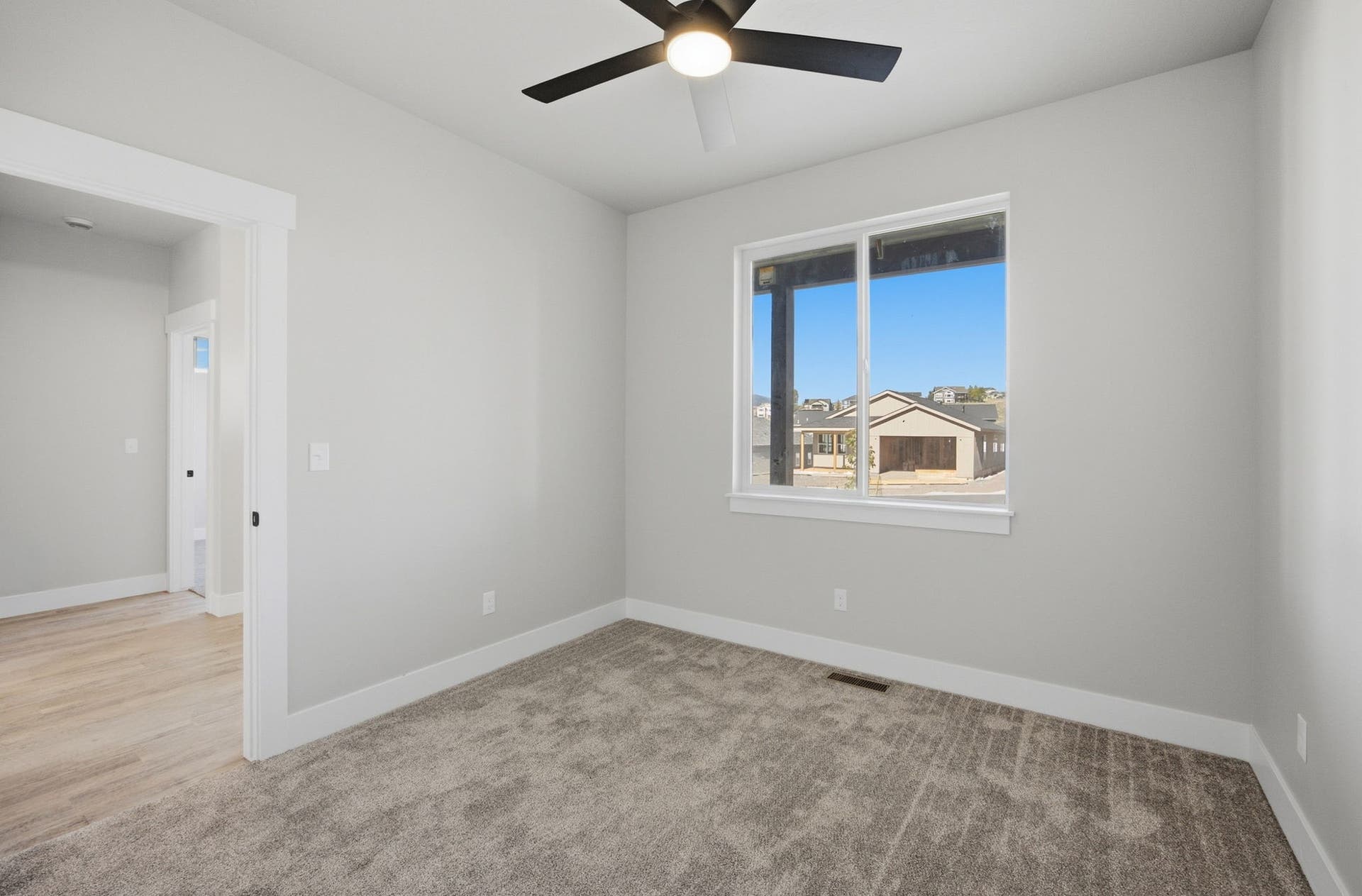 Neutral-toned carpeting, single window with white trim, modern ceiling fan, white wall paint, and white door trim
