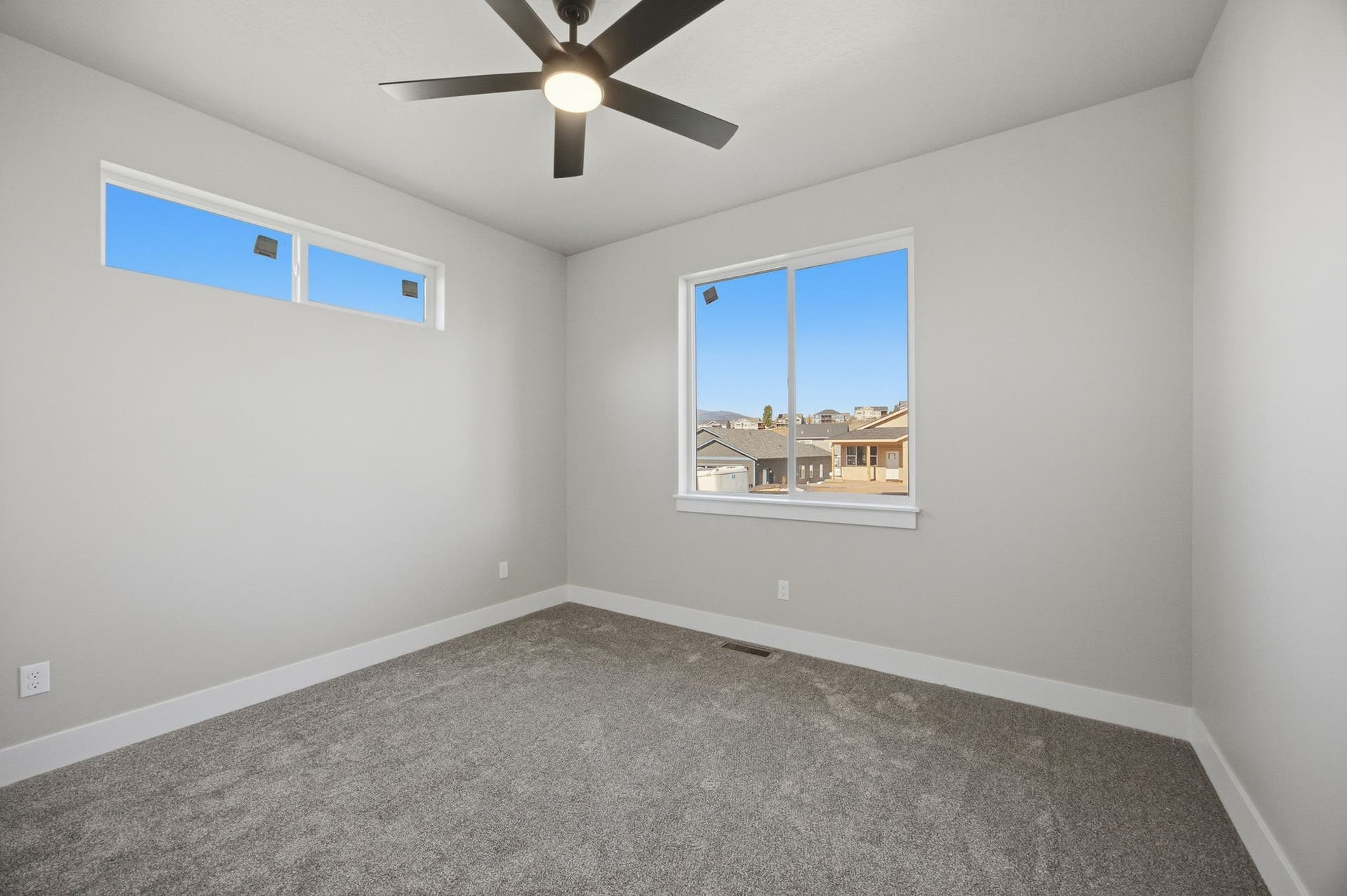 Neutral wall tones, gray carpeting, a contemporary ceiling fan, and multiple windows providing natural illumination