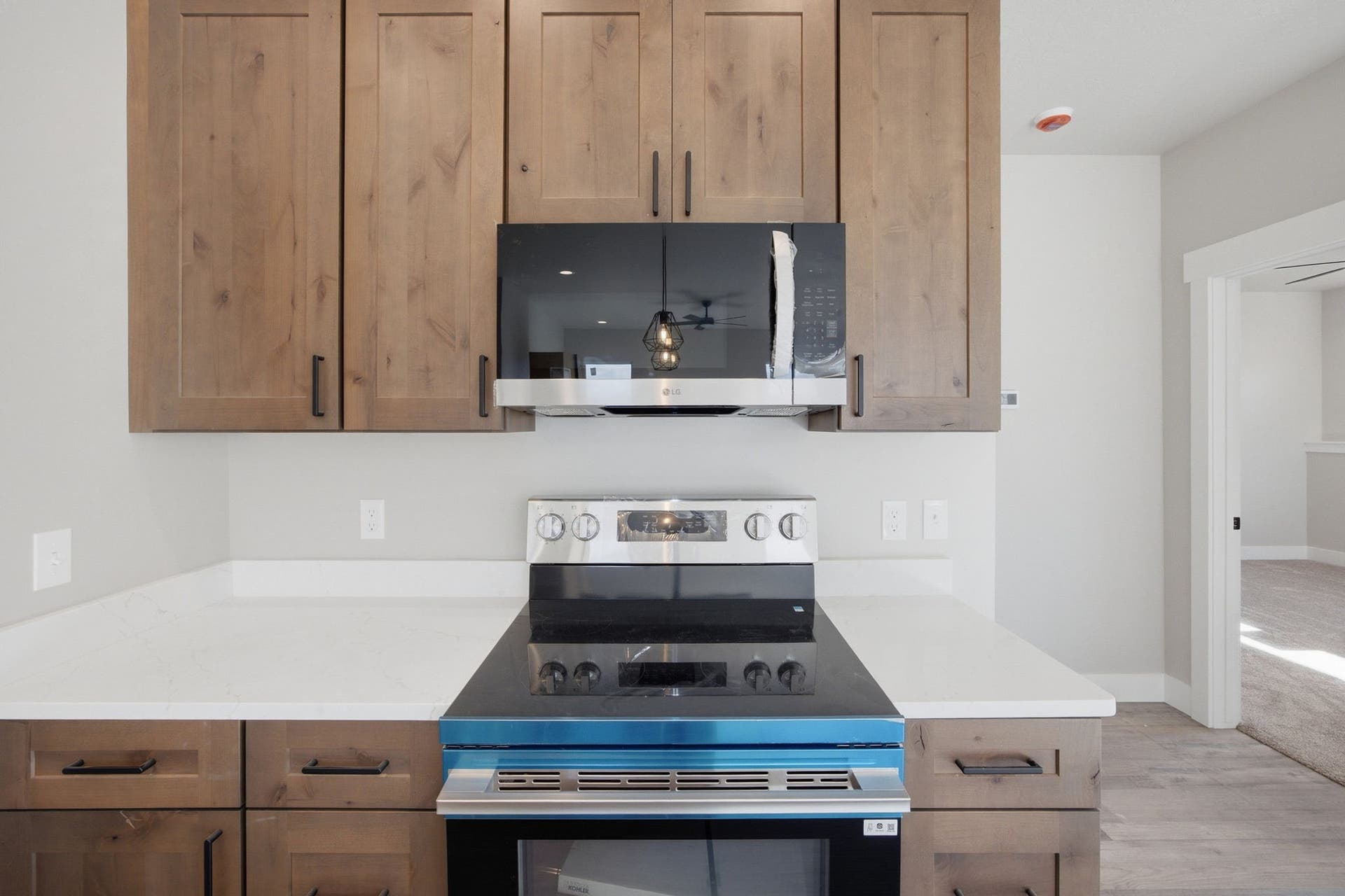 Wood-finish cabinetry with matte black hardware, white countertops, built-in microwave, and stainless steel range