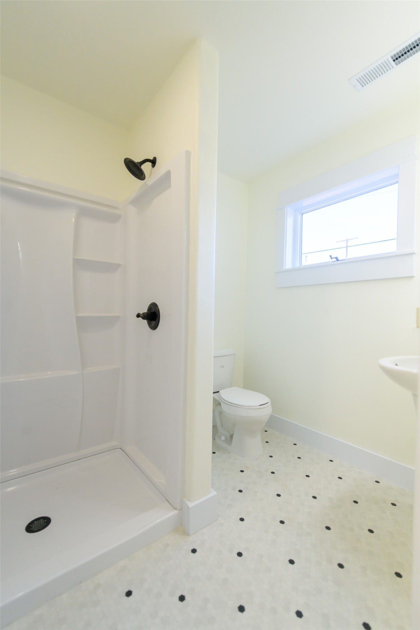 705 W Park Street, Butte, MT 59701 White shower stall with dark bronze fixtures, white hexagon tile flooring with dark accent dots, and a single pane window