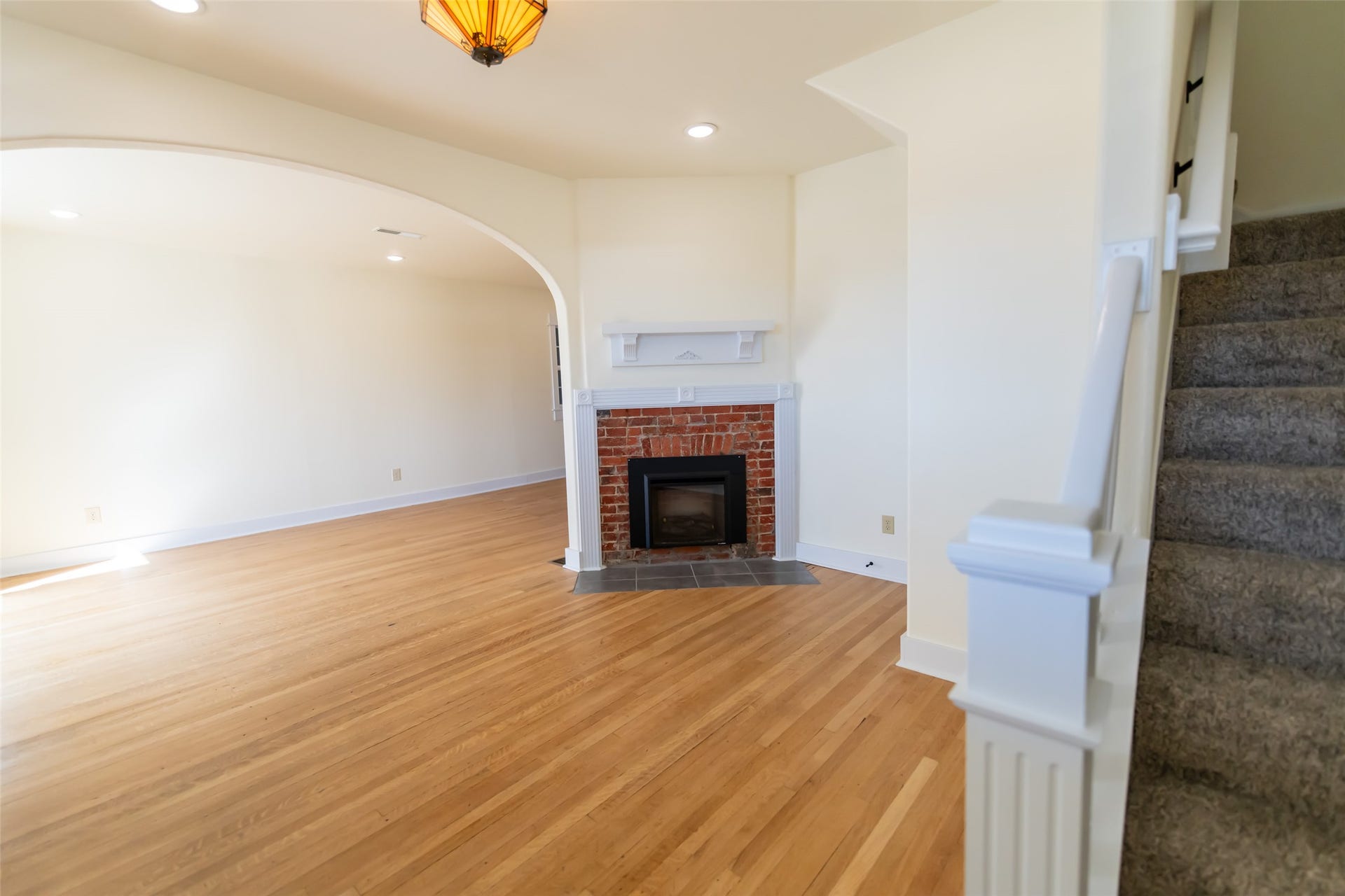 705 W Park Street, Butte, MT 59701 Hardwood flooring throughout, brick-surround fireplace with hearth, an arched doorway, recessed lighting, and a staircase with carpeting