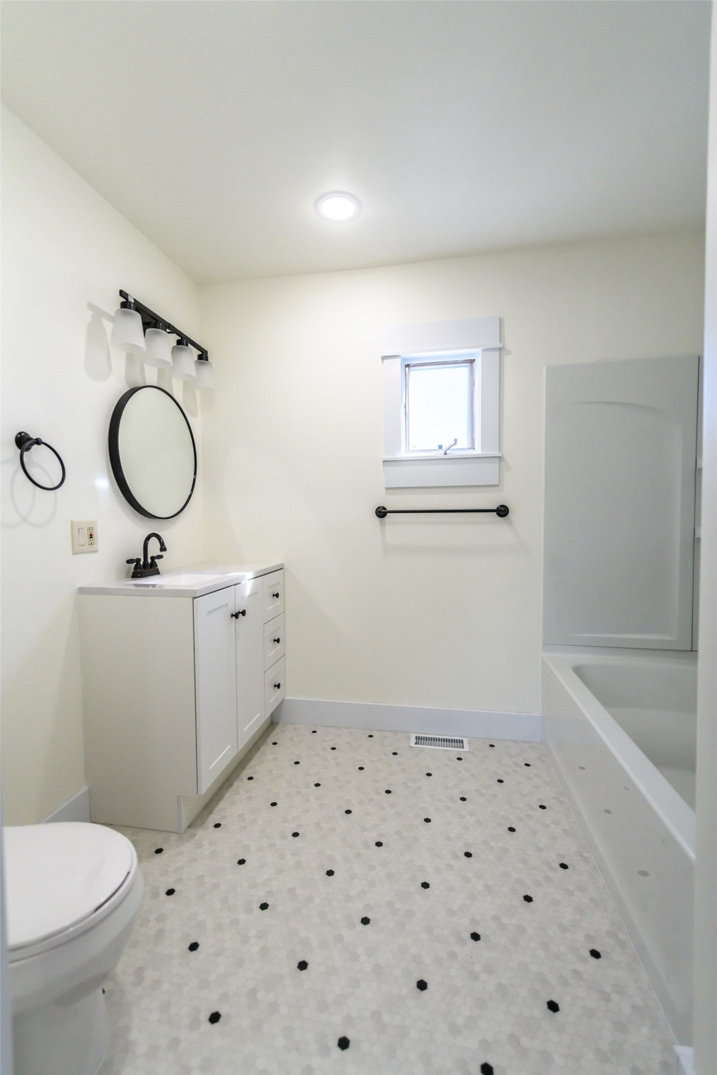 705 W Park Street, Butte, MT 59701 White hexagonal tile flooring with black accents, white vanity with black hardware, round black-framed mirror, contemporary black light fixture, and a white bathtub