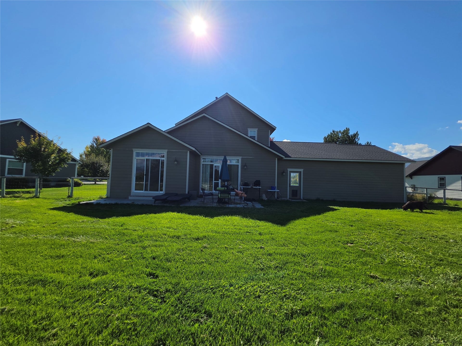 585 Wildflower Circle, Hamilton, MT 59840 Expansive green lawn, rear patio, sliding glass doors, exterior siding, and a durable roof