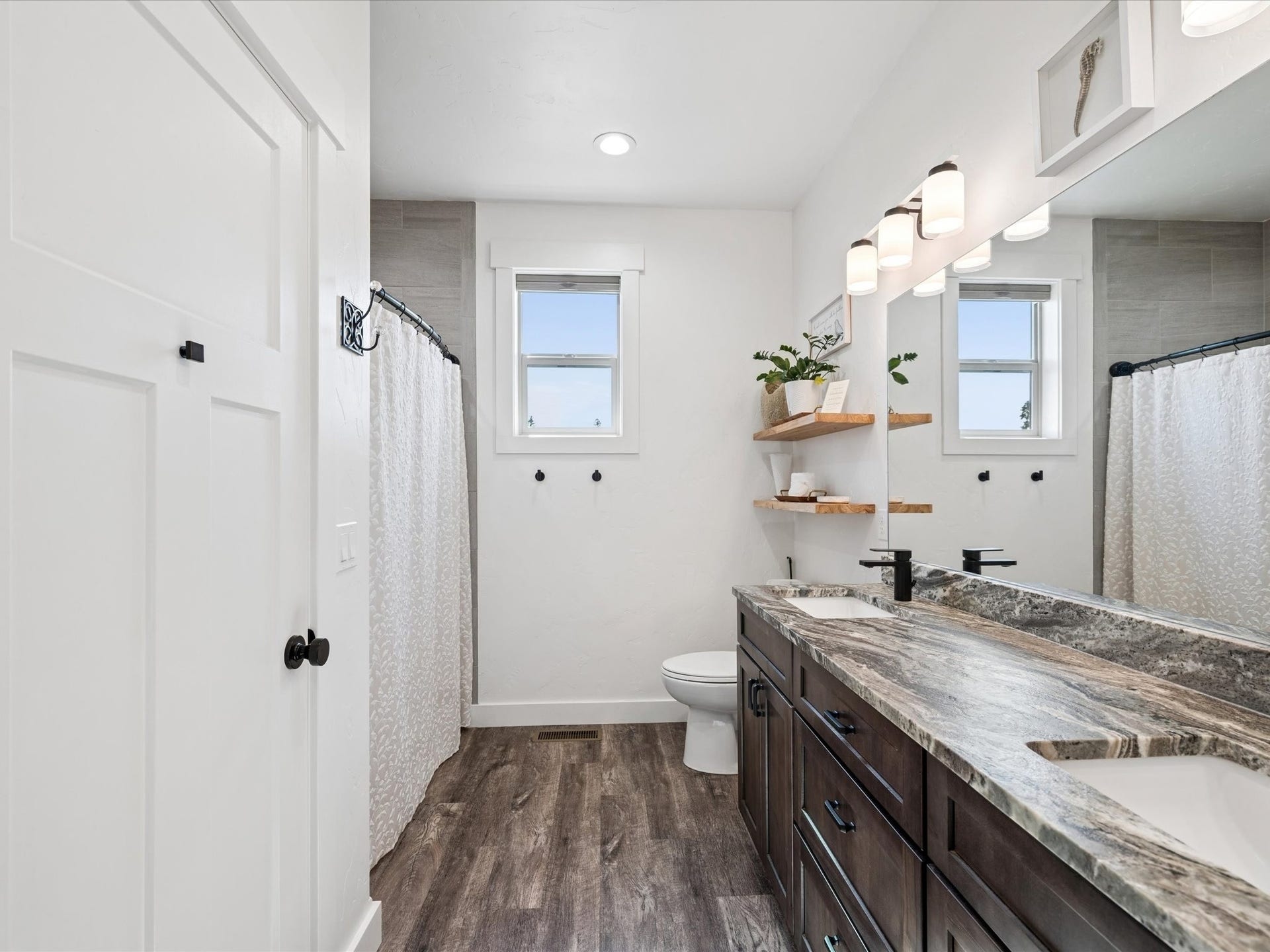 148 Fox Den Trail, Kalispell, MT 59901 Wood-finish flooring, window, dark wood vanity with dual sinks, wall-mounted light fixture, and floor-to-ceiling tiled shower, granite countertop