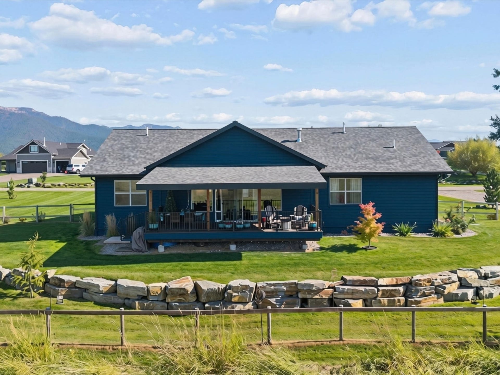 148 Fox Den Trail, Kalispell, MT 59901 Expansive backyard featuring a covered deck, manicured lawn, and a stone retaining wall