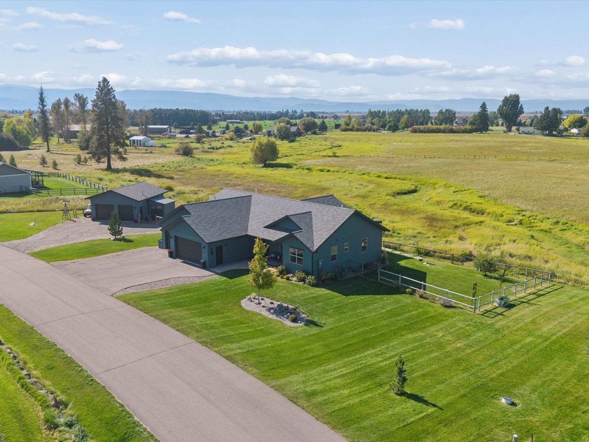 148 Fox Den Trail, Kalispell, MT 59901 Exterior with a dark gray roof, attached garage, detached shop, paved driveway, and manicured lawn