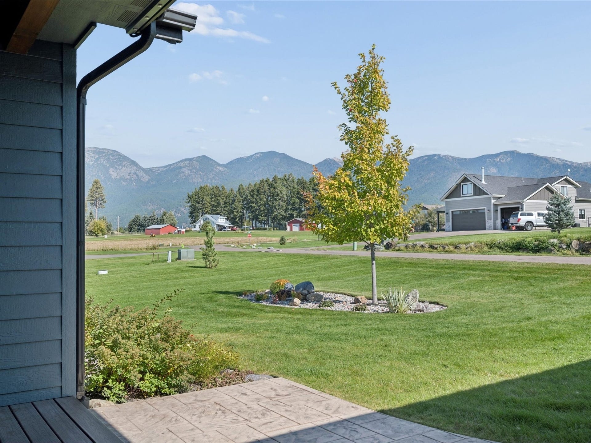 148 Fox Den Trail, Kalispell, MT 59901 Stamped concrete porch with a manicured lawn, established landscaping, and mountain backdrop