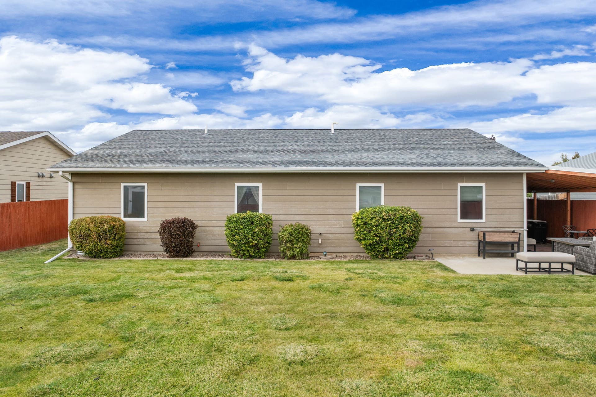 2541 Castle Pines Way, Great Falls, MT 59405 Expansive lawn space, tan horizontal siding, white-trimmed windows, concrete patio, and a covered patio area