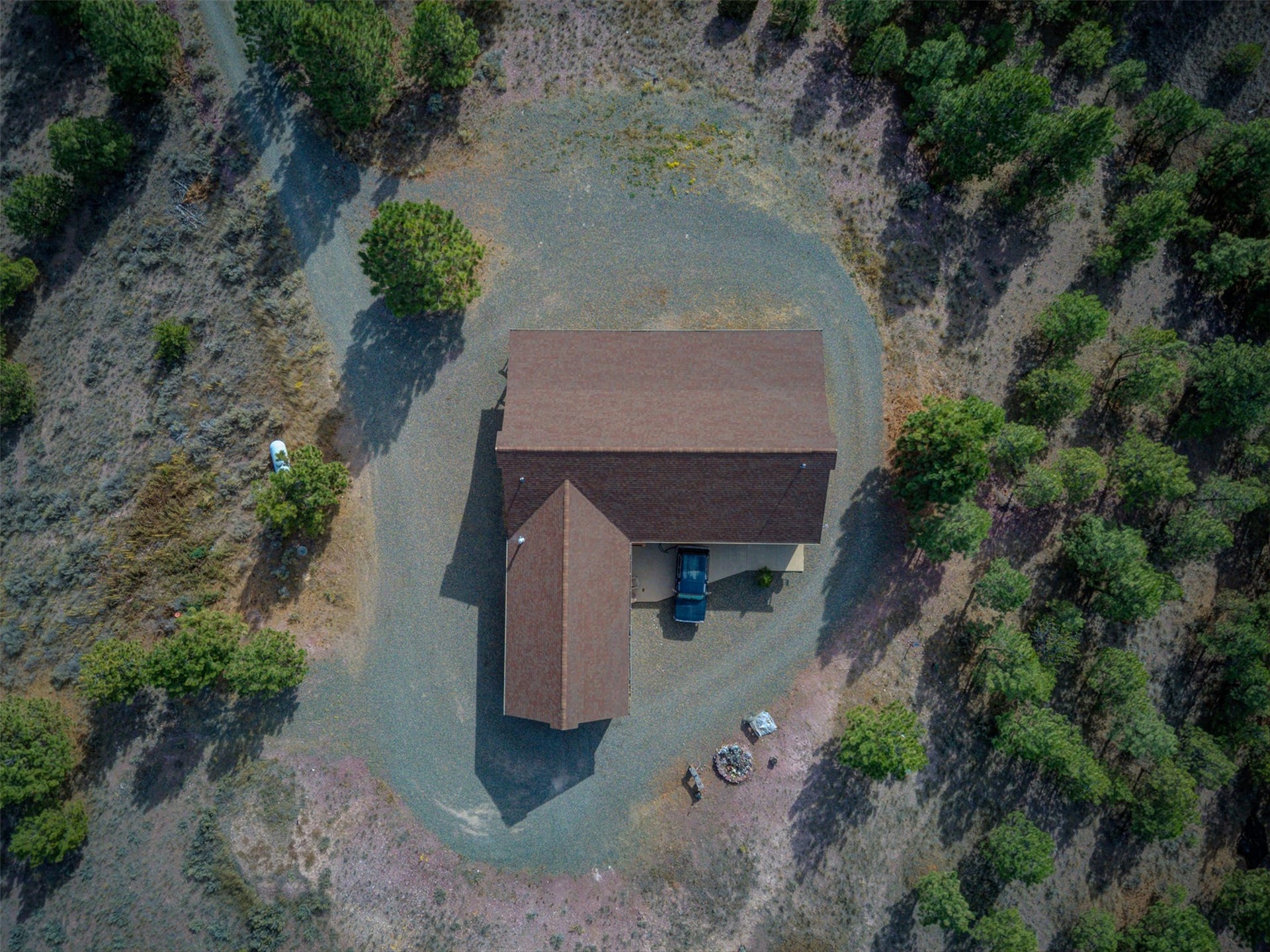 8224 Hillside Drive, Helena, MT 59602 L-shaped structure with brown roofing, surrounded by natural landscaping, featuring a gravel driveway and a fire pit area