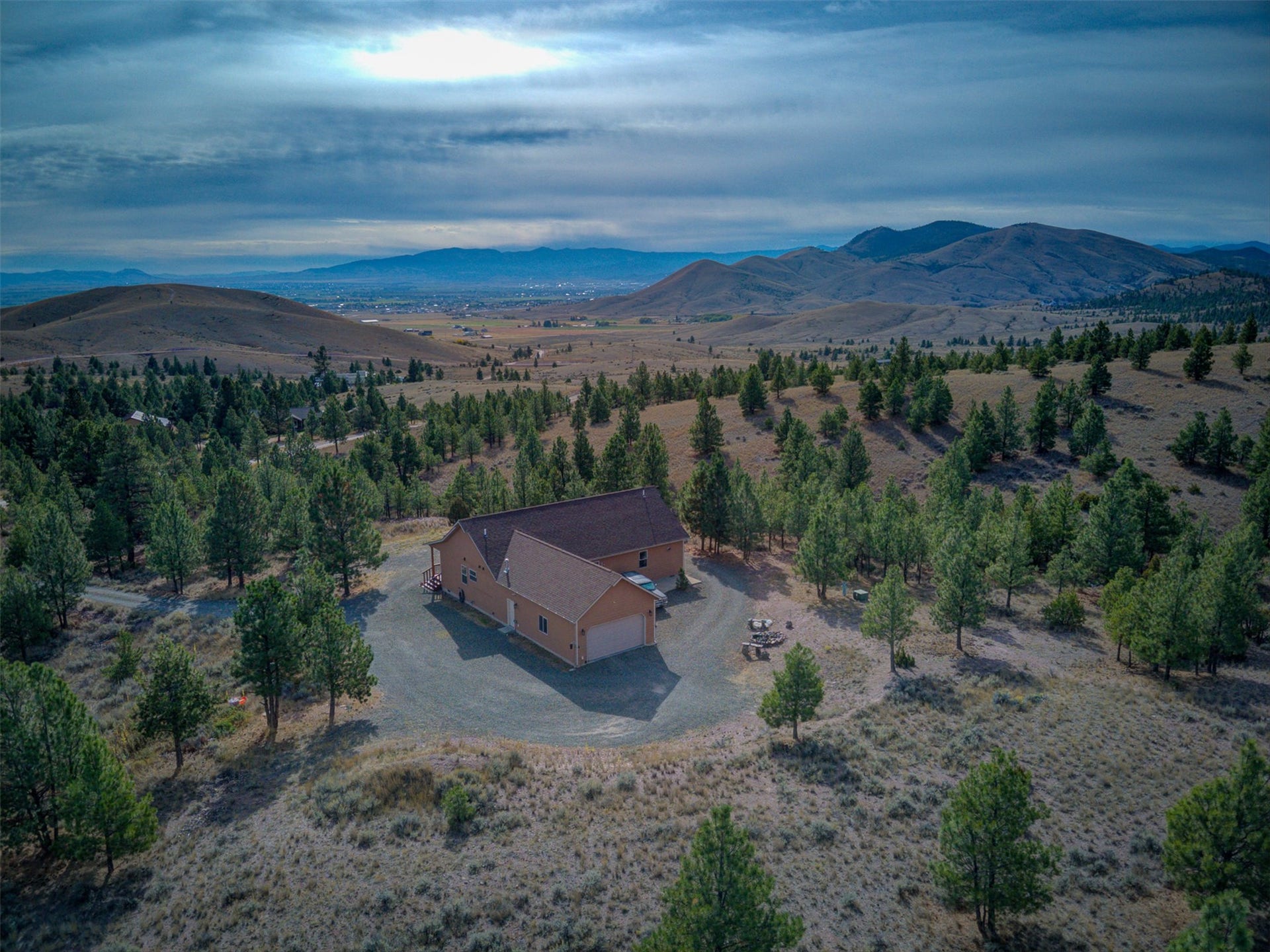 8224 Hillside Drive, Helena, MT 59602 Expansive property with a tan-sided residence, attached garage, surrounding evergreen trees, and a gravel driveway