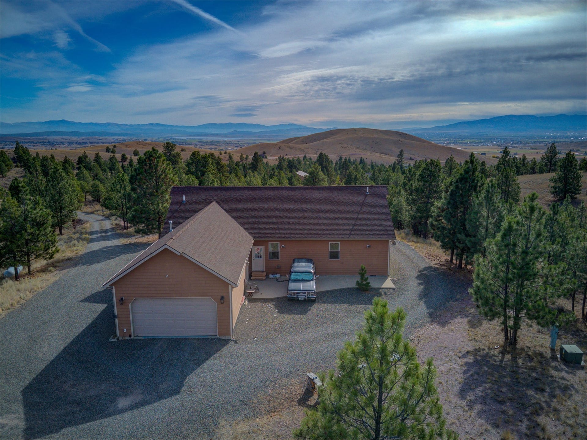 8224 Hillside Drive, Helena, MT 59602 Siding exterior with attached garage, surrounded by mature trees, and a mountain backdrop