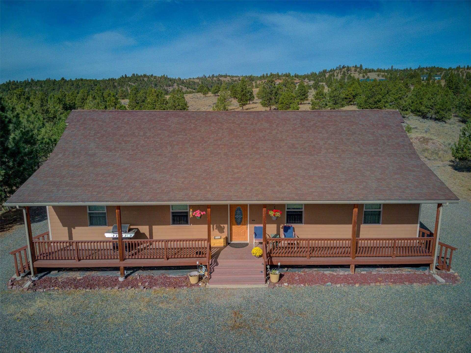 8224 Hillside Drive, Helena, MT 59602 Expansive front porch with dark wood-finish railings, set against a backdrop of mature trees and a distant mountain range