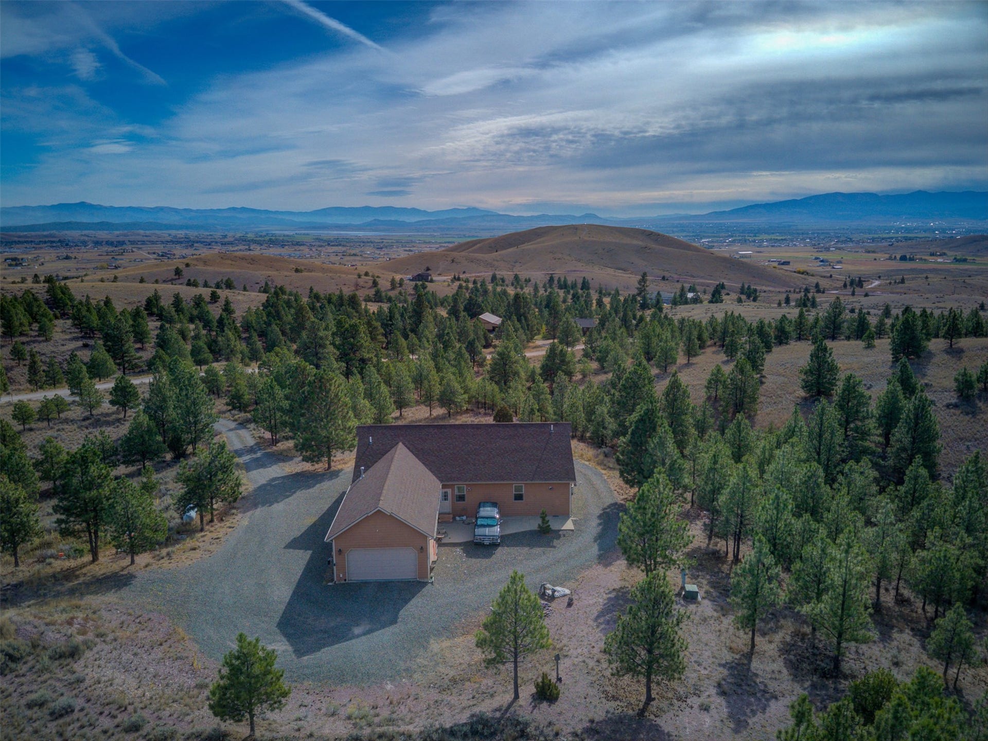 8224 Hillside Drive, Helena, MT 59602 Expansive property featuring a brown exterior, attached two-car garage, gravel driveway, and surrounding mature conifer trees