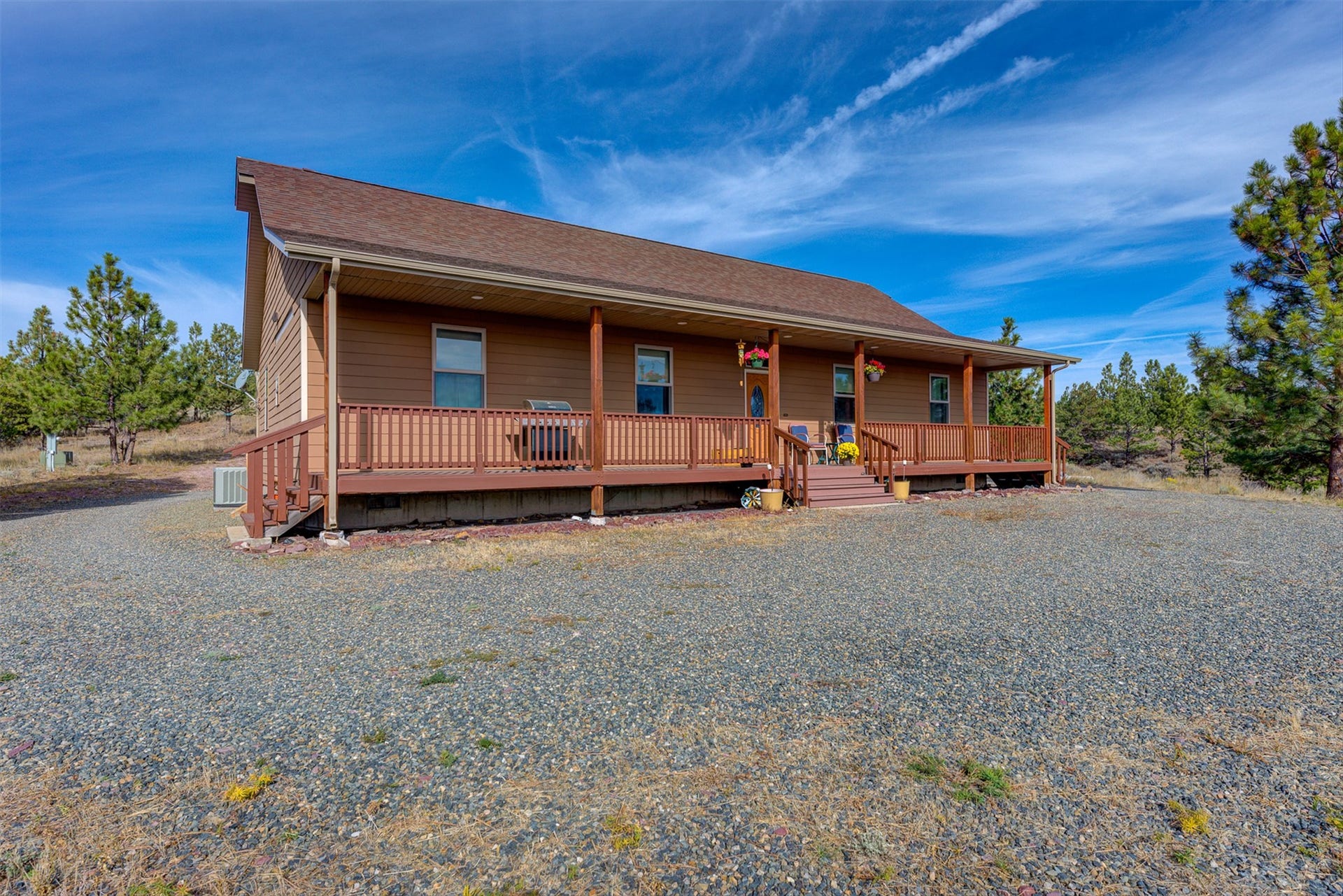 8224 Hillside Drive, Helena, MT 59602 Brown siding exterior with a full-length covered porch, dark wood railings, and a gravel driveway