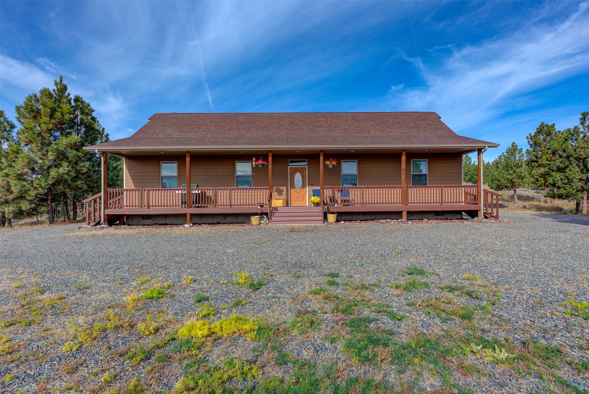 8224 Hillside Drive, Helena, MT 59602 Ranch-style residence featuring a prominent covered porch with railing, a brown shingle roof, and a gravel driveway