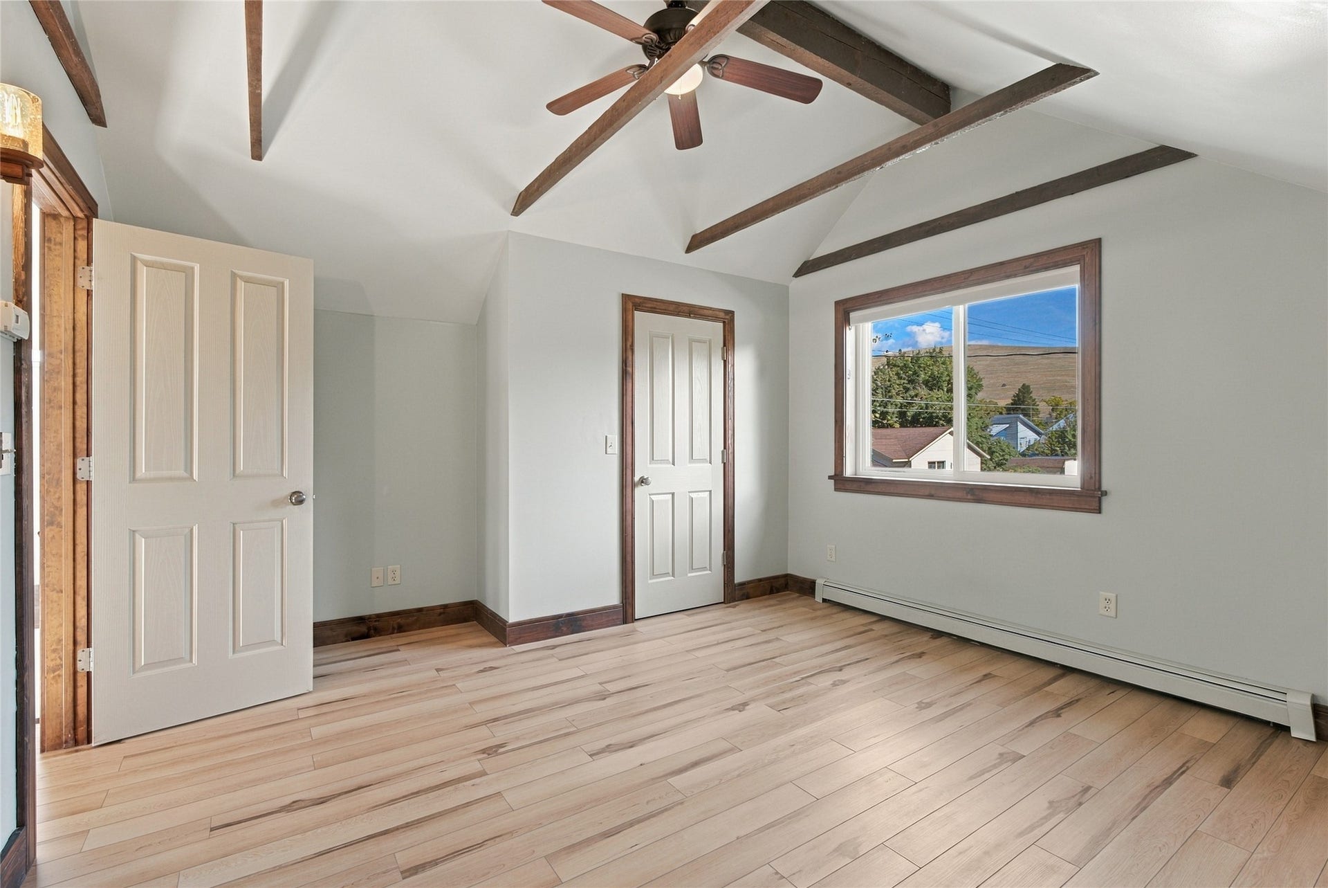 Vaulted ceiling with exposed wood beams, wood-finish flooring, ceiling fan with integrated lighting, and a window with exterior scenery