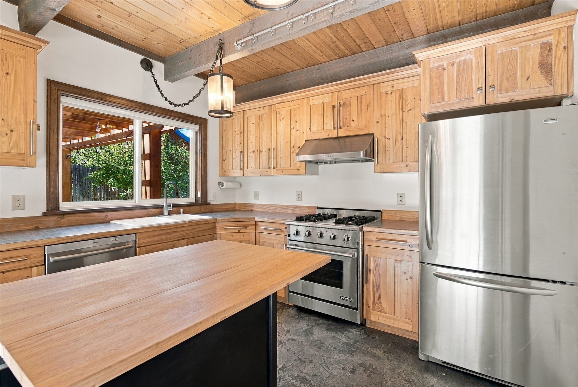 Wood-paneled ceiling with exposed beams, wood cabinetry, stainless steel appliances, and a wood-top island