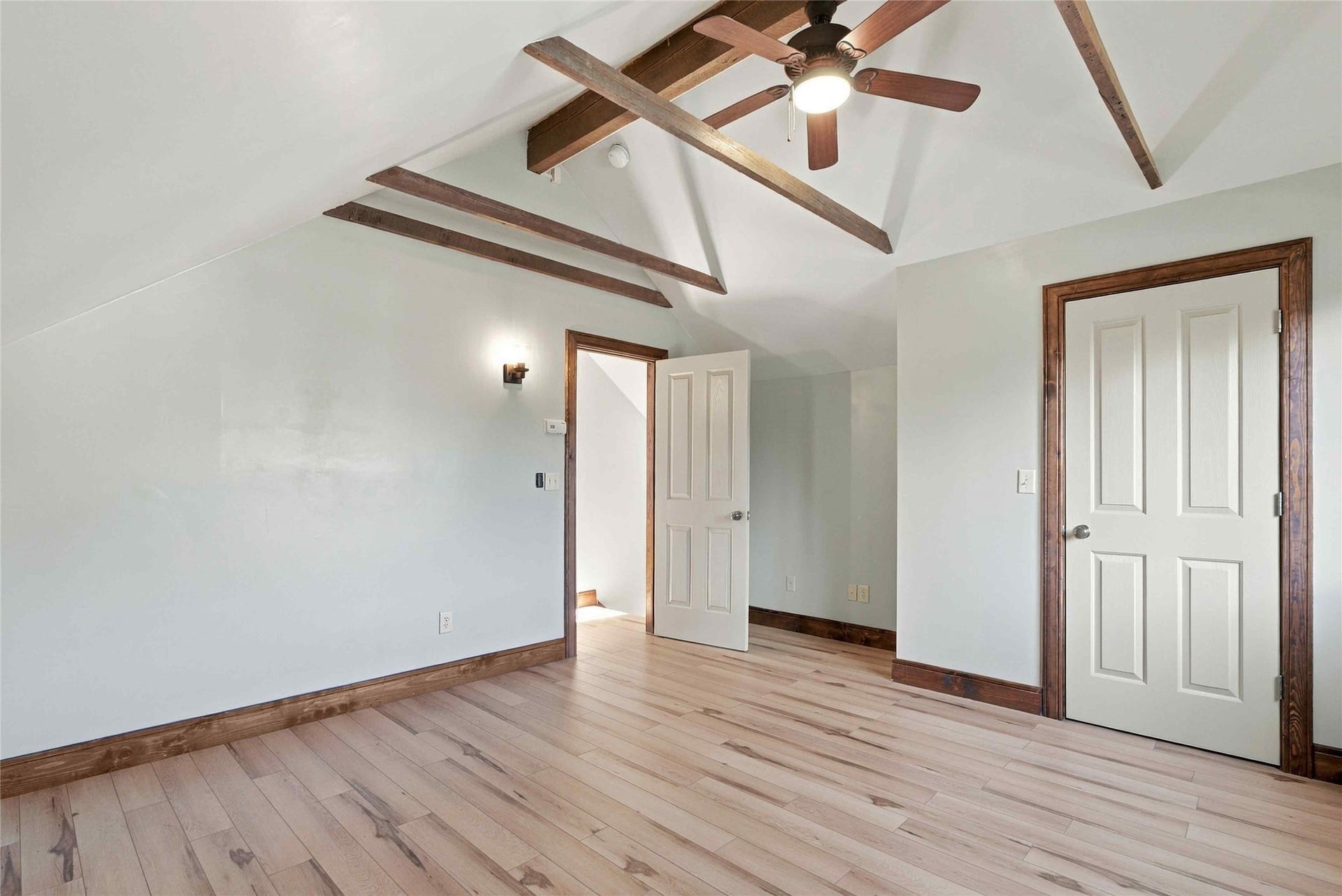 Vaulted ceiling featuring exposed wood beams, a ceiling fan with integrated lighting, light wood-finish flooring, and white paneled doors with dark wood trim
