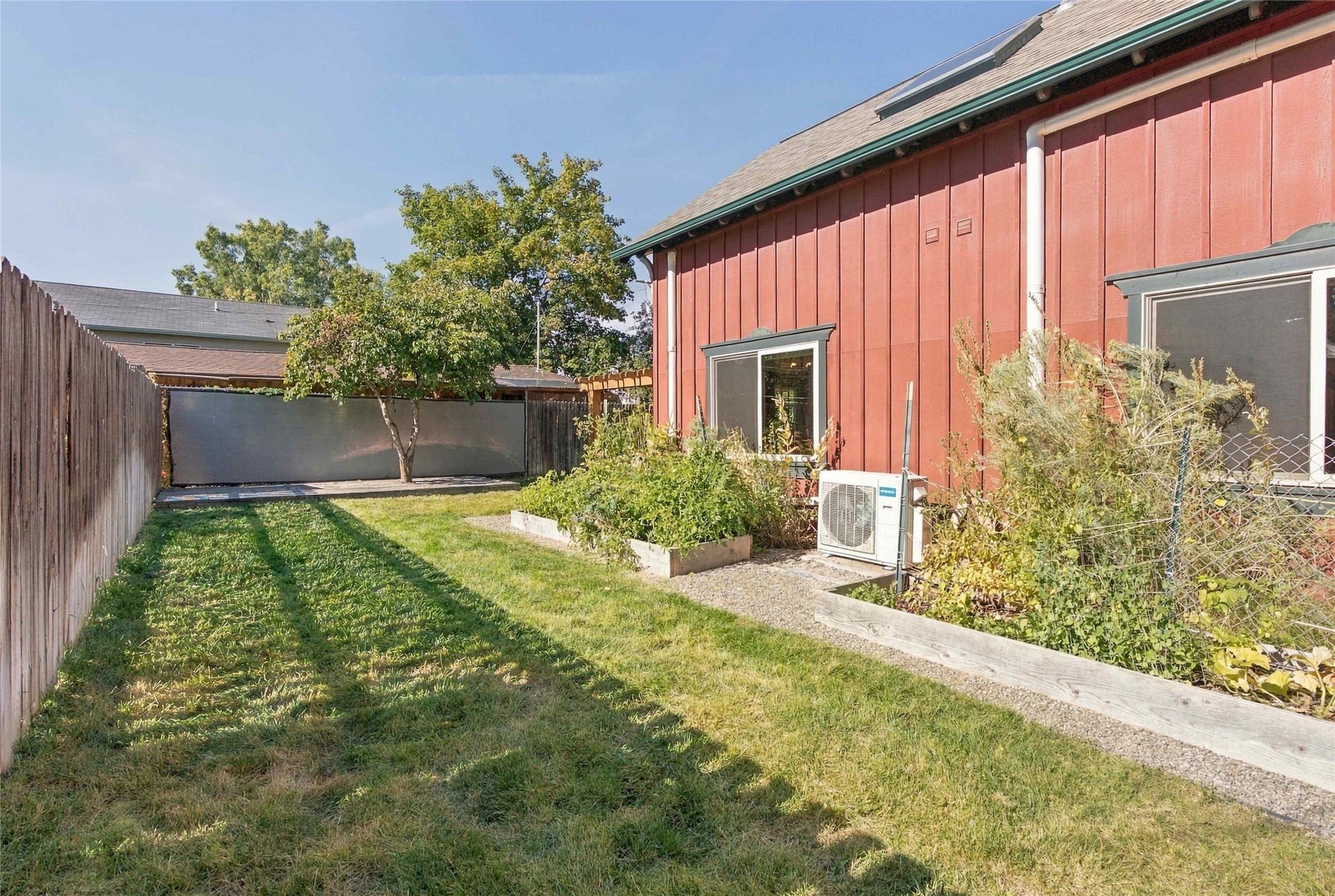 Grassed area with a wood fence, mature tree, raised garden bed, and a red exterior wall with multiple windows